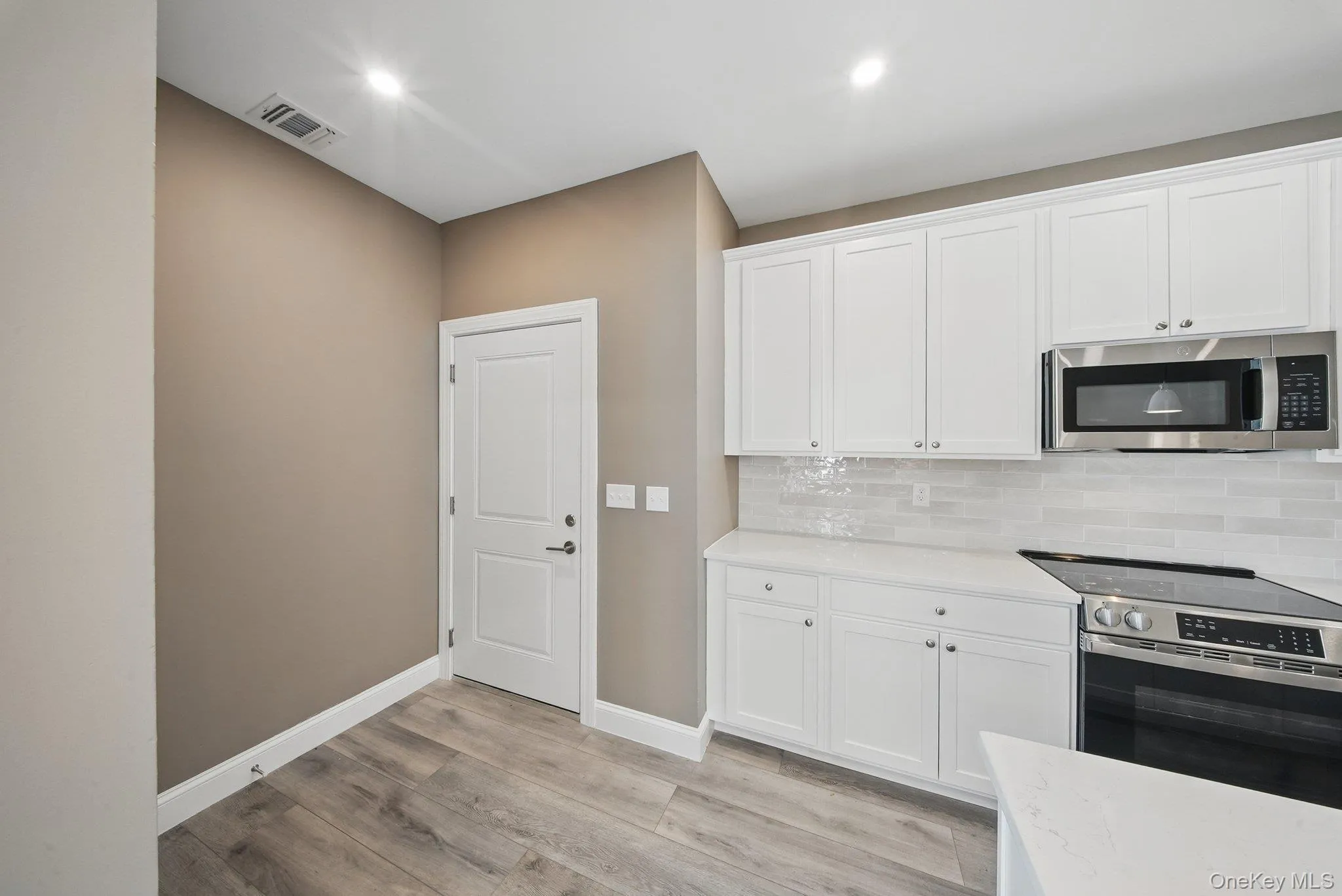 Kitchen with white cabinets, stainless steel appliances, decorative backsplash, light wood-style flooring, and light stone countertops Kitchen with white cabinets, stainless steel appliances, decorative backsplash, light wood-style flooring, and light stone countertops