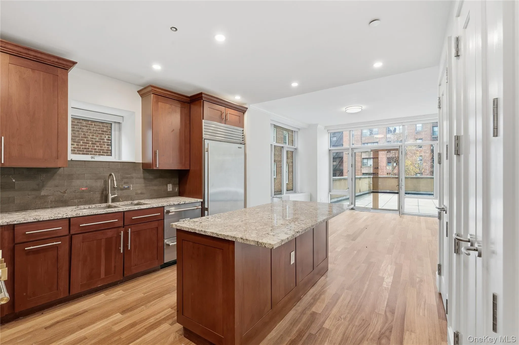 Kitchen with decorative backsplash, light wood-style flooring, light stone countertops, a kitchen island, and recessed lighting Kitchen with decorative backsplash, light wood-style flooring, light stone countertops, a kitchen island, and recessed lighting