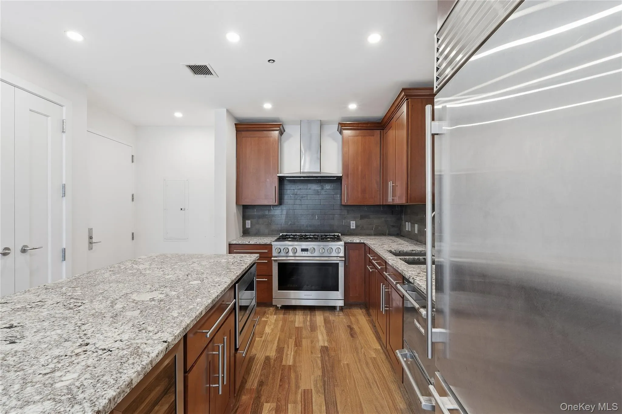 Kitchen with appliances with stainless steel finishes, light wood finished floors, light stone countertops, decorative backsplash, and recessed lighting Kitchen with appliances with stainless steel finishes, light wood finished floors, light stone countertops, decorative backsplash, and recessed lighting