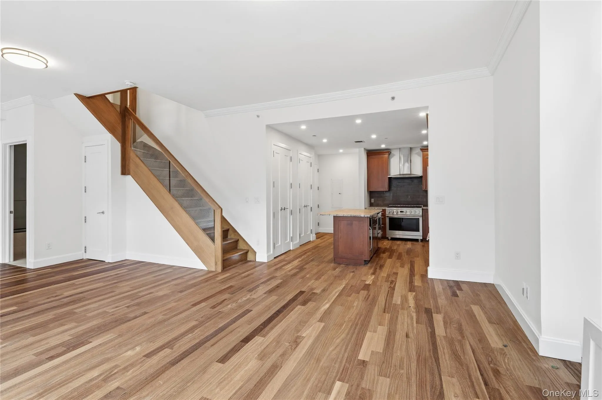 Unfurnished living room with ornamental molding, light wood-style flooring, stairway, and recessed lighting Unfurnished living room with ornamental molding, light wood-style flooring, stairway, and recessed lighting