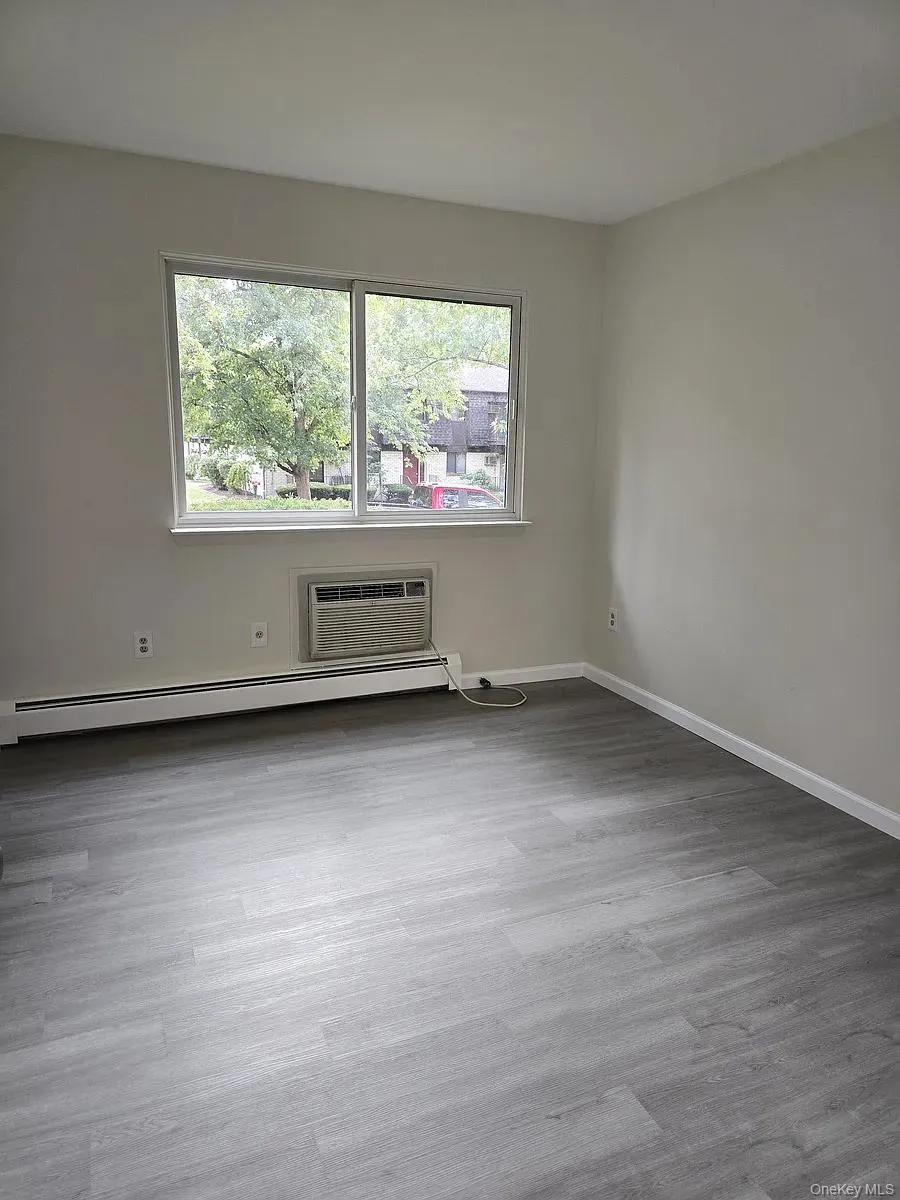 Empty room with light wood-style floors, baseboard heating, and a wall mounted AC Empty room with light wood-style floors, baseboard heating, and a wall mounted AC