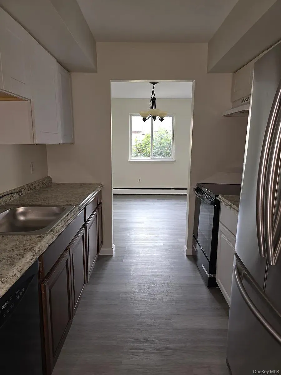 Kitchen featuring black appliances, dark wood-style flooring, white cabinetry, decorative light fixtures, and under cabinet range hood Kitchen featuring black appliances, dark wood-style flooring, white cabinetry, decorative light fixtures, and under cabinet range hood