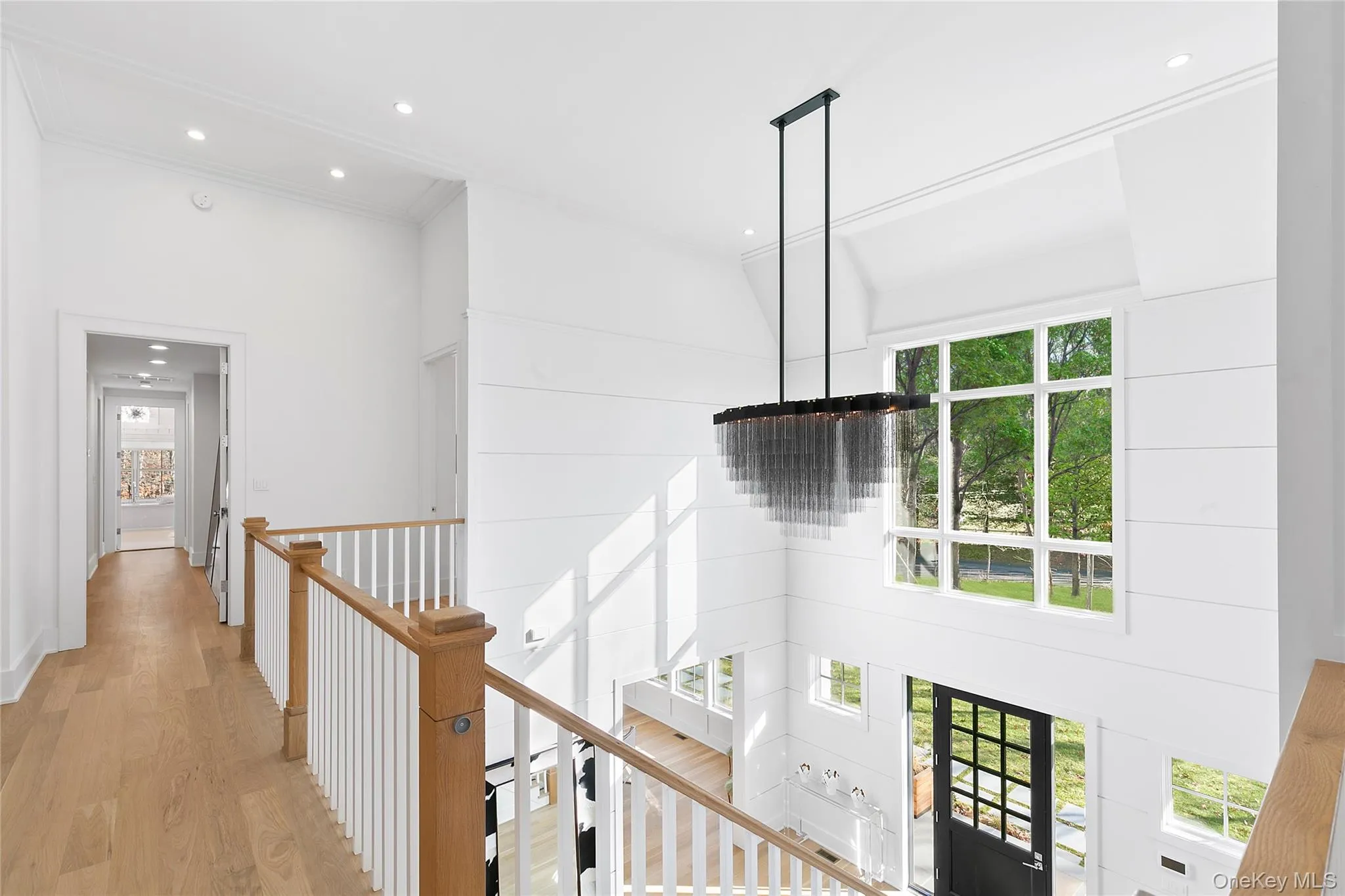 Corridor featuring recessed lighting, light wood-type flooring, a towering ceiling, ornamental molding, and a chandelier Corridor featuring recessed lighting, light wood-type flooring, a towering ceiling, ornamental molding, and a chandelier