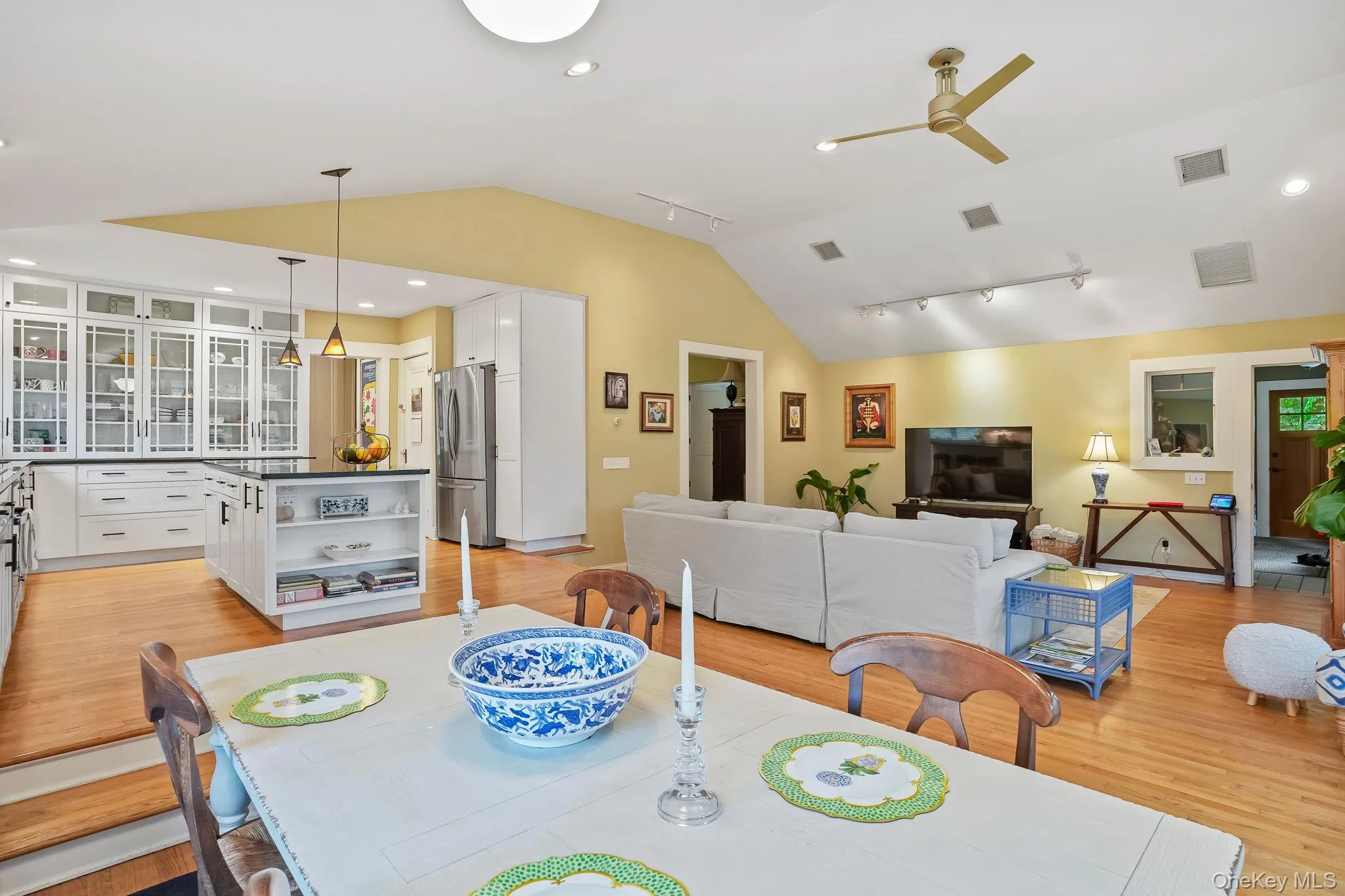 Dining area open to kitchen and great room with vaulted ceiling, rail lighting, light wood finished floors, recessed lighting, and a ceiling fan Dining area open to kitchen and great room with vaulted ceiling, rail lighting, light wood finished floors, recessed lighting, and a ceiling fan