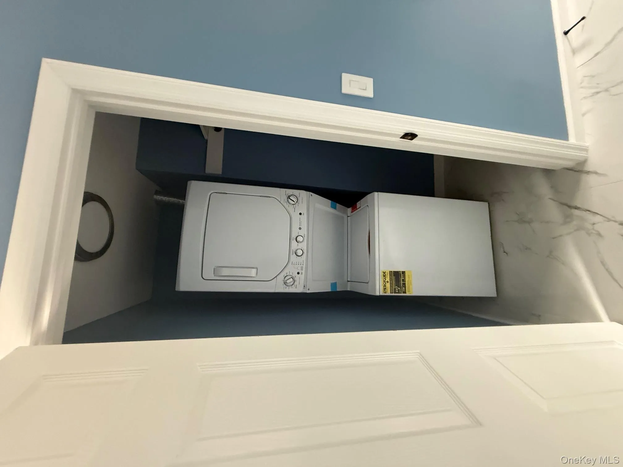 Laundry room featuring light marble finish flooring and estacked washer and dryer Laundry room featuring light marble finish flooring and estacked washer and dryer
