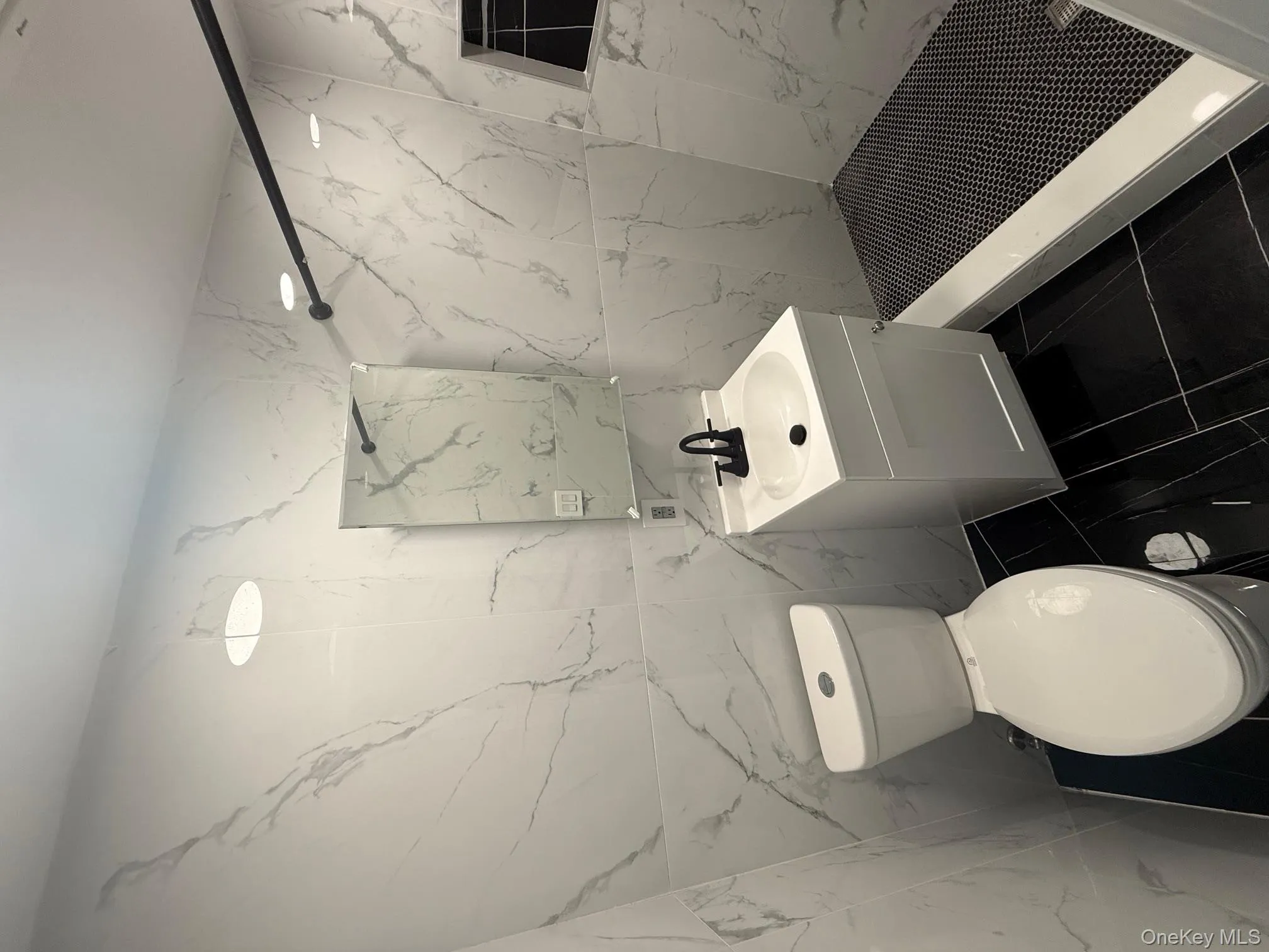 Full bathroom featuring a marble finish shower, tile walls, vanity, stone wall, and dark tile patterned flooring Full bathroom featuring a marble finish shower, tile walls, vanity, stone wall, and dark tile patterned flooring