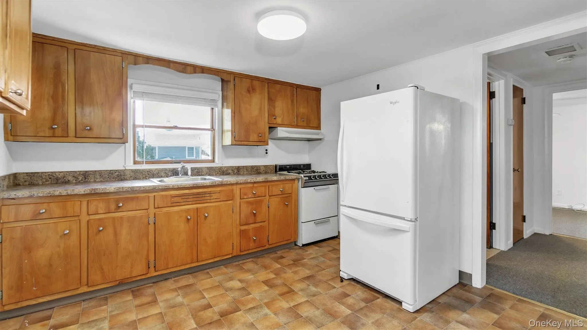 Kitchen featuring white appliances, brown cabinets, and under cabinet range hood Kitchen featuring white appliances, brown cabinets, and under cabinet range hood