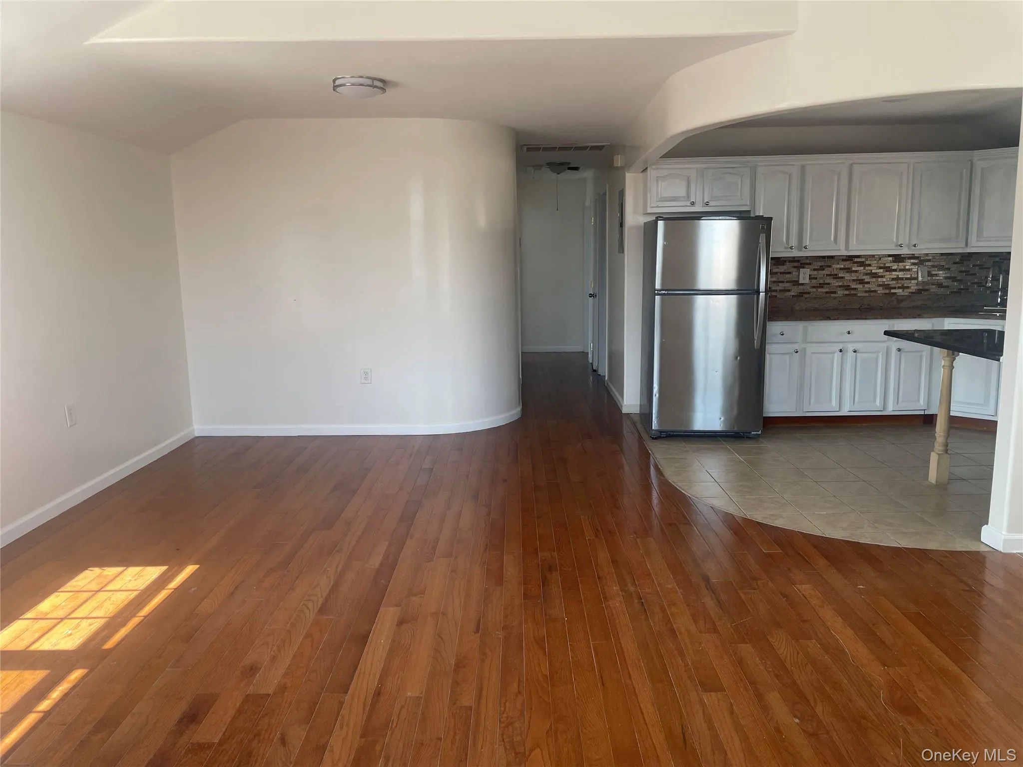 Kitchen with dark countertops, freestanding refrigerator, backsplash, white cabinetry, and light wood finished floors Kitchen with dark countertops, freestanding refrigerator, backsplash, white cabinetry, and light wood finished floors