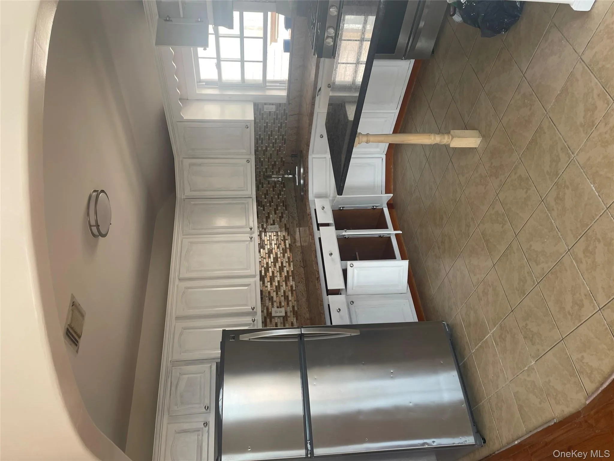 Kitchen featuring fridge, white cabinets, range, tasteful backsplash, and light tile patterned flooring Kitchen featuring fridge, white cabinets, range, tasteful backsplash, and light tile patterned flooring