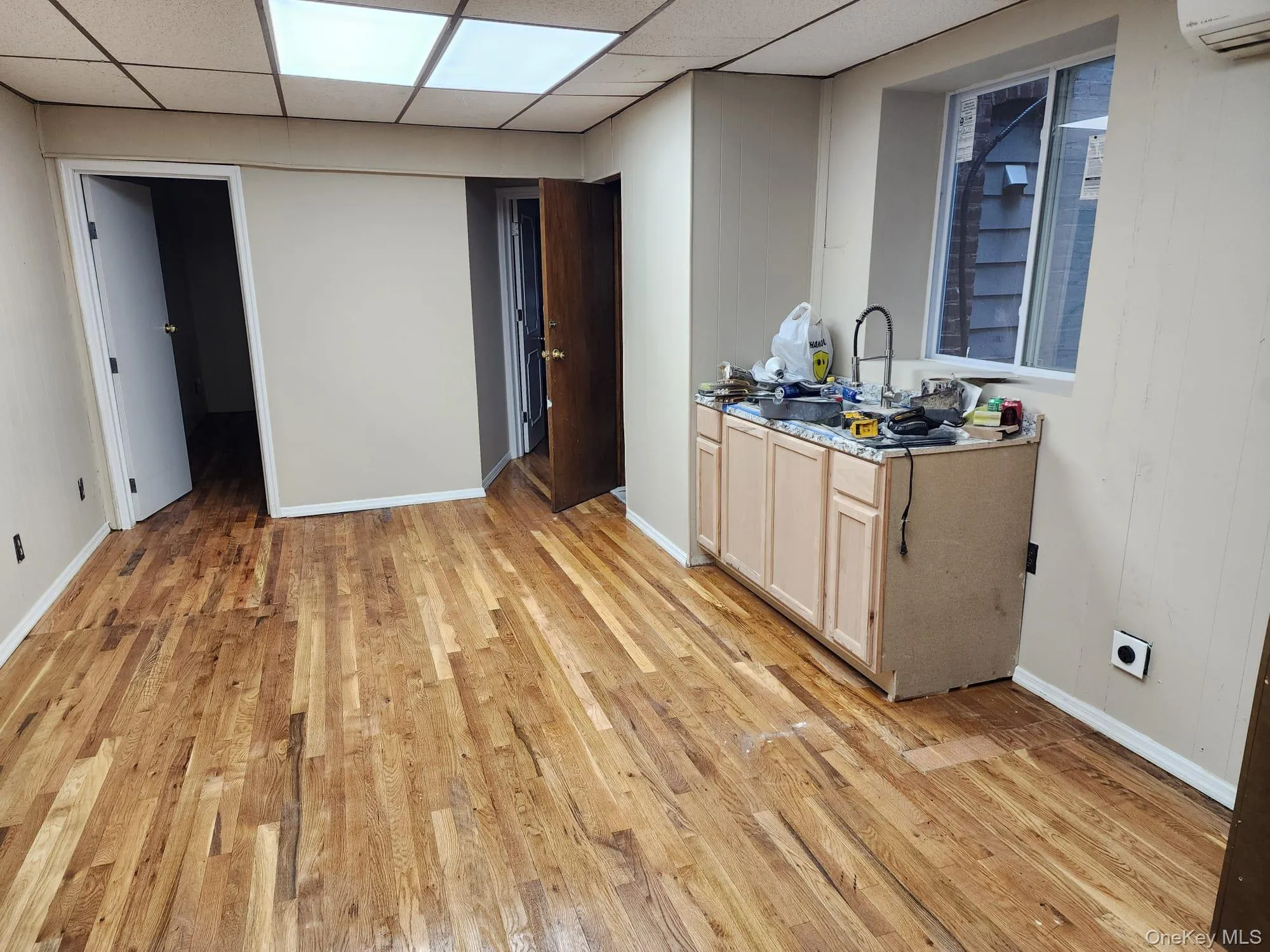 Kitchen with a drop ceiling, light wood-style flooring, light brown cabinetry, and a wall mounted air conditioner Kitchen with a drop ceiling, light wood-style flooring, light brown cabinetry, and a wall mounted air conditioner