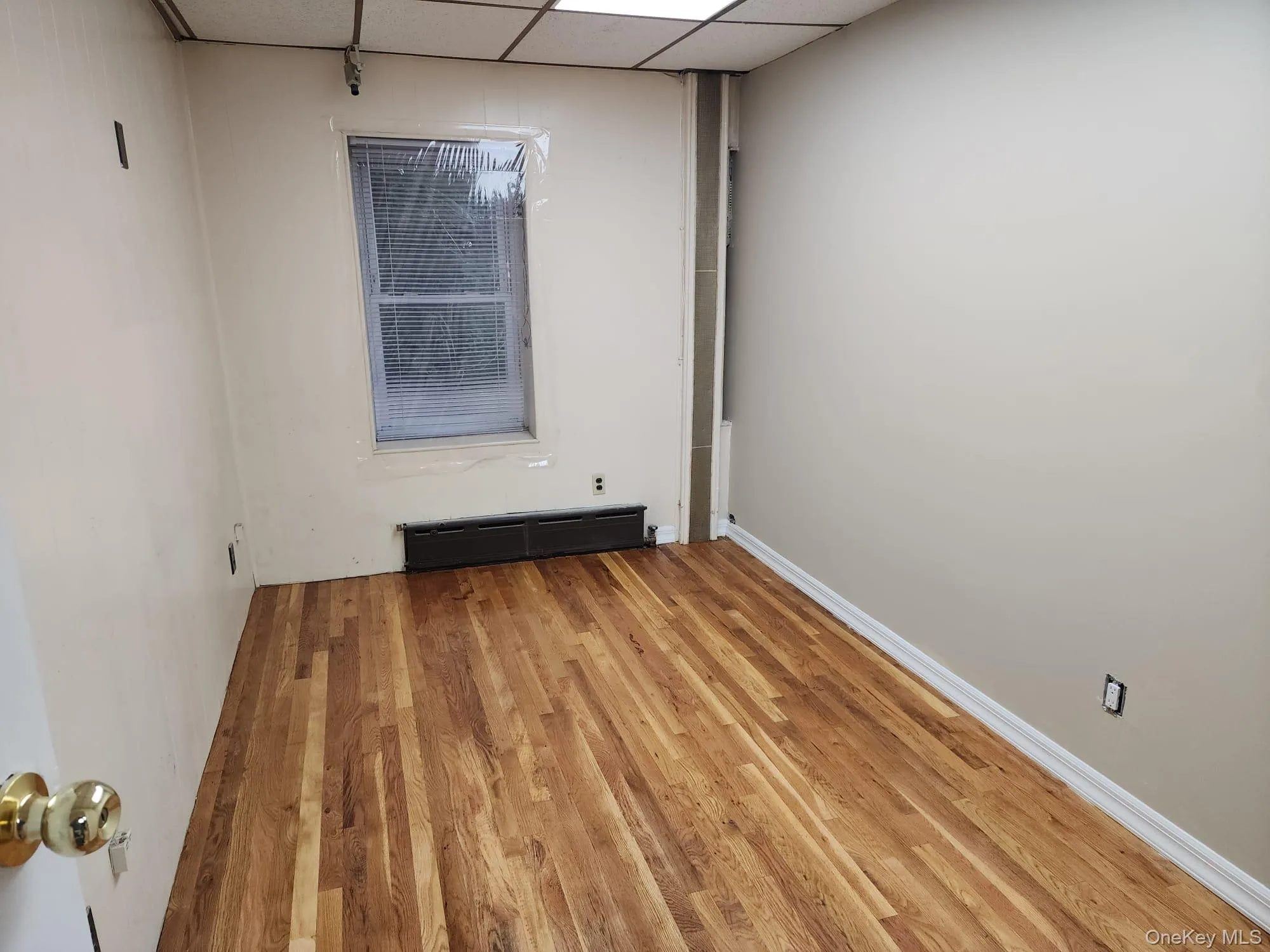 Spare room featuring a drop ceiling, wood finished floors, and a baseboard radiator Spare room featuring a drop ceiling, wood finished floors, and a baseboard radiator