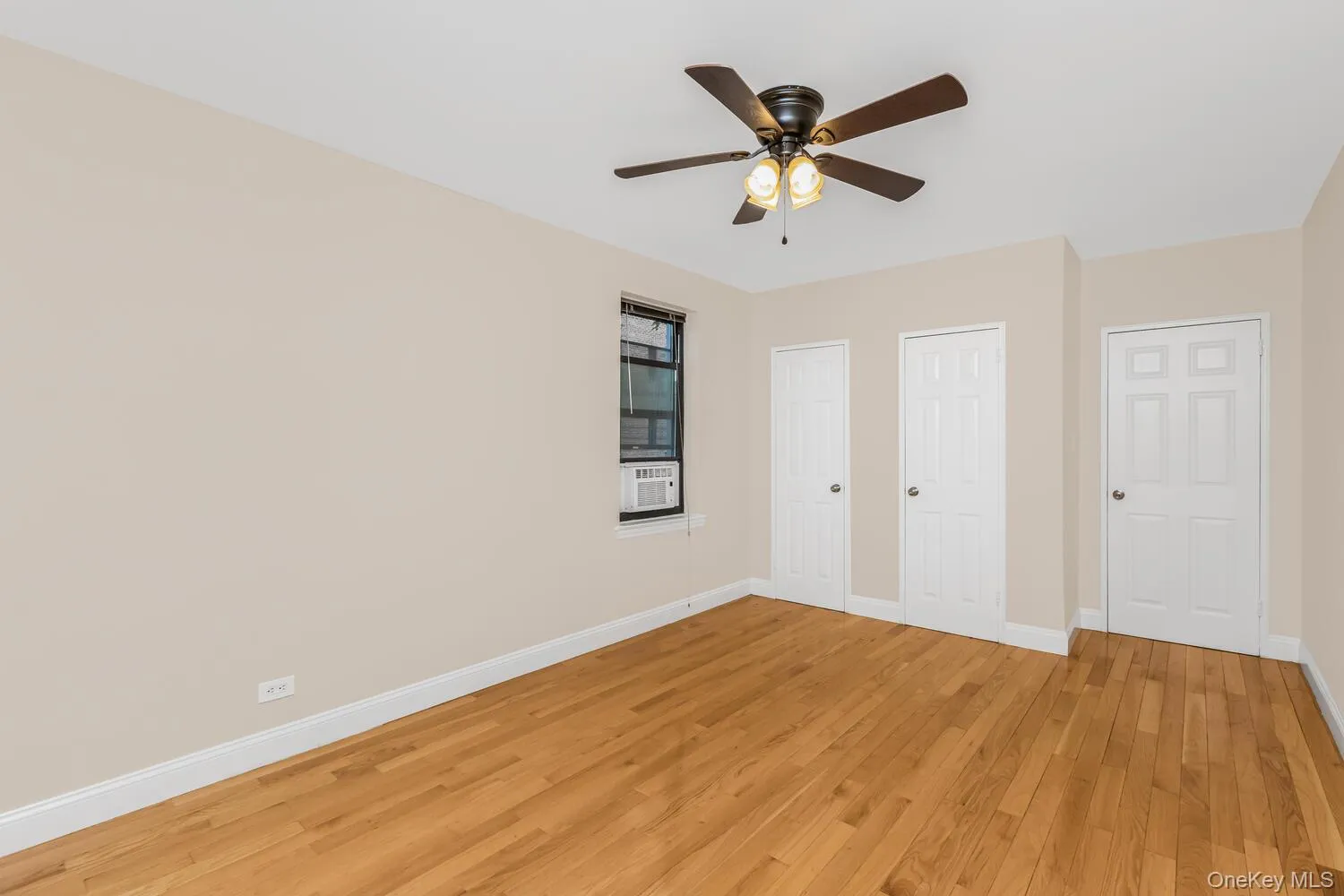 Unfurnished bedroom featuring wood finished floors, multiple closets, a ceiling fan, and cooling unit Unfurnished bedroom featuring wood finished floors, multiple closets, a ceiling fan, and cooling unit
