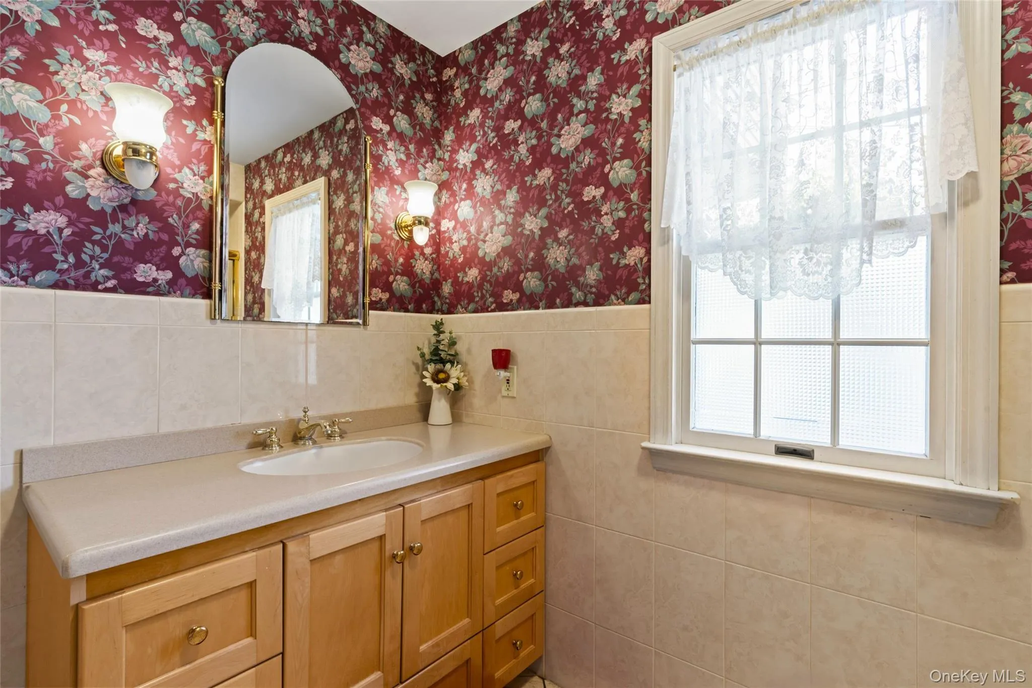 Bathroom featuring plenty of natural light, vanity, tile walls, a wainscoted wall, and wallpapered walls Bathroom featuring plenty of natural light, vanity, tile walls, a wainscoted wall, and wallpapered walls