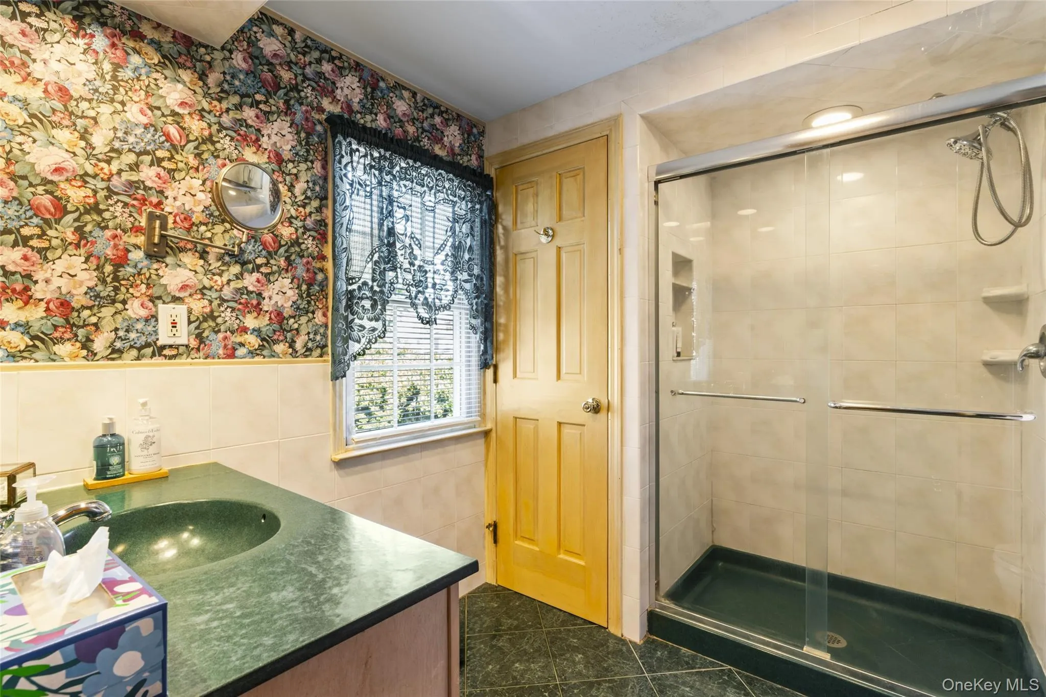 Full bath featuring vanity, tile walls, wallpapered walls, dark tile patterned flooring, and a stall shower Full bath featuring vanity, tile walls, wallpapered walls, dark tile patterned flooring, and a stall shower
