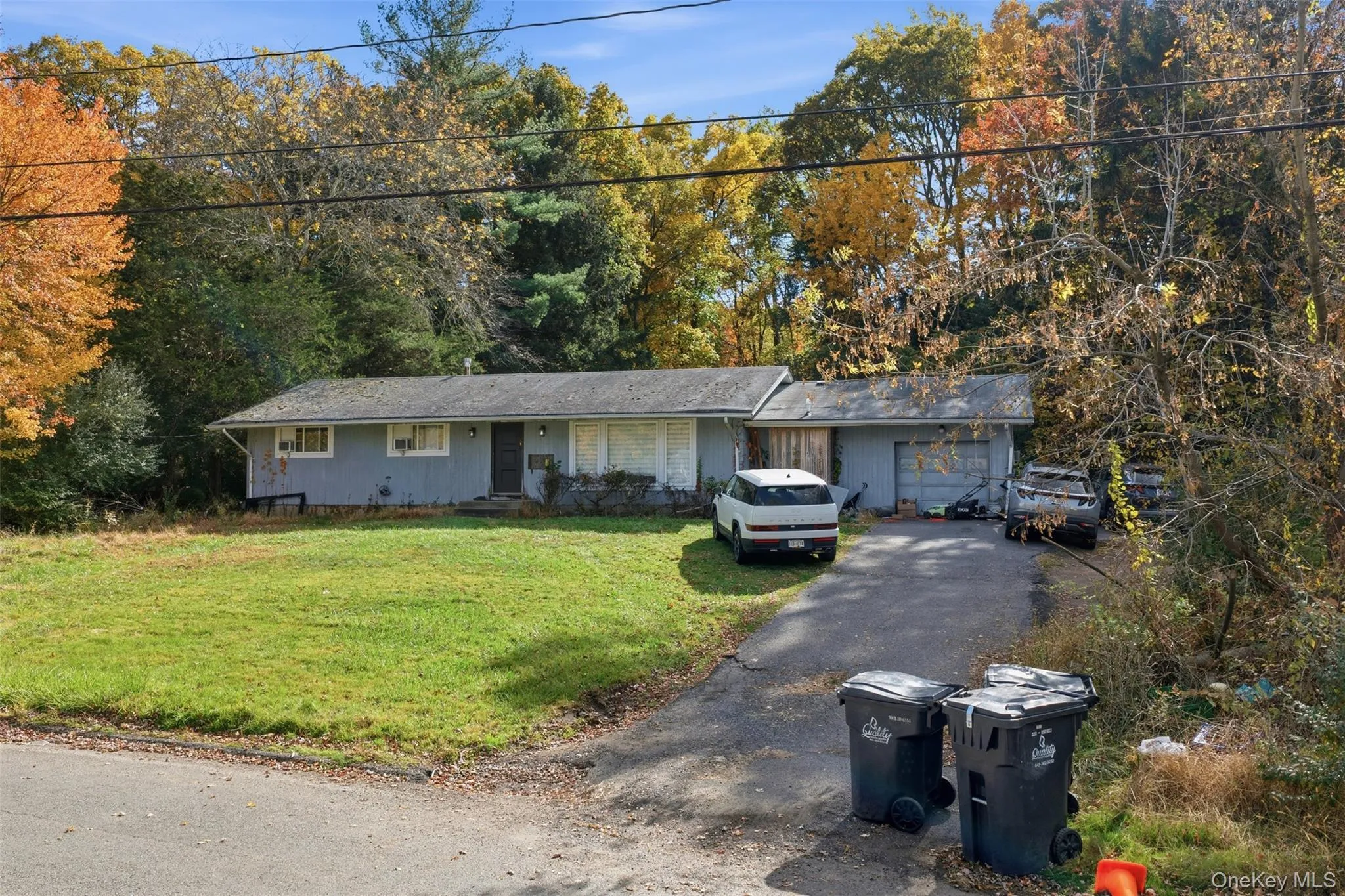 Ranch-style house featuring a front lawn, asphalt driveway, view of scattered trees, and a garage Ranch-style house featuring a front lawn, asphalt driveway, view of scattered trees, and a garage