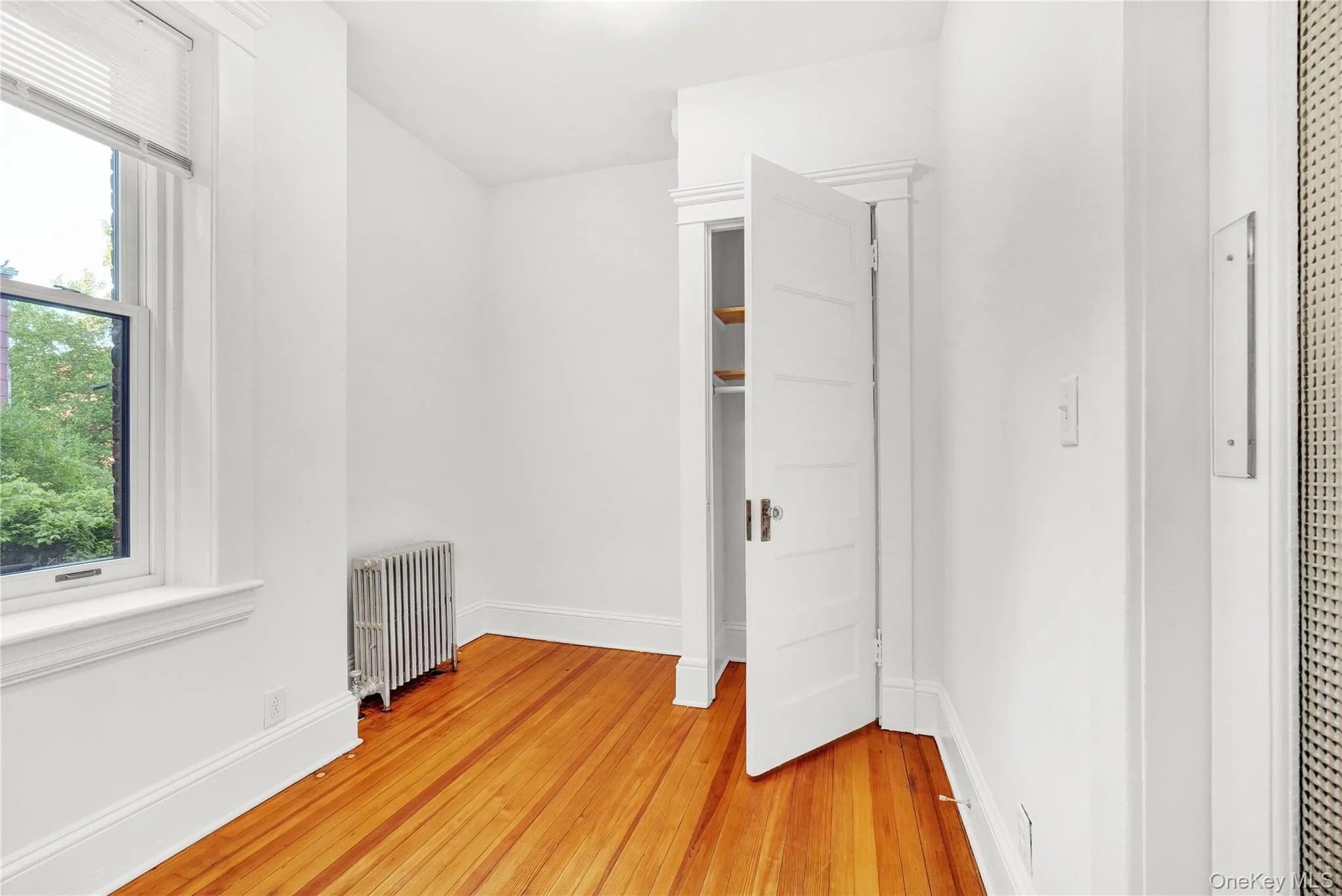 Walk in closet featuring radiator and light wood finished floors Walk in closet featuring radiator and light wood finished floors