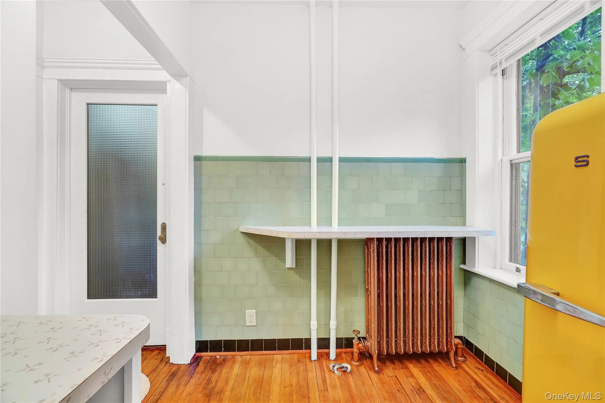 Kitchen featuring tile walls, radiator, hardwood / wood-style floors, wainscoting, and light countertops Kitchen featuring tile walls, radiator, hardwood / wood-style floors, wainscoting, and light countertops
