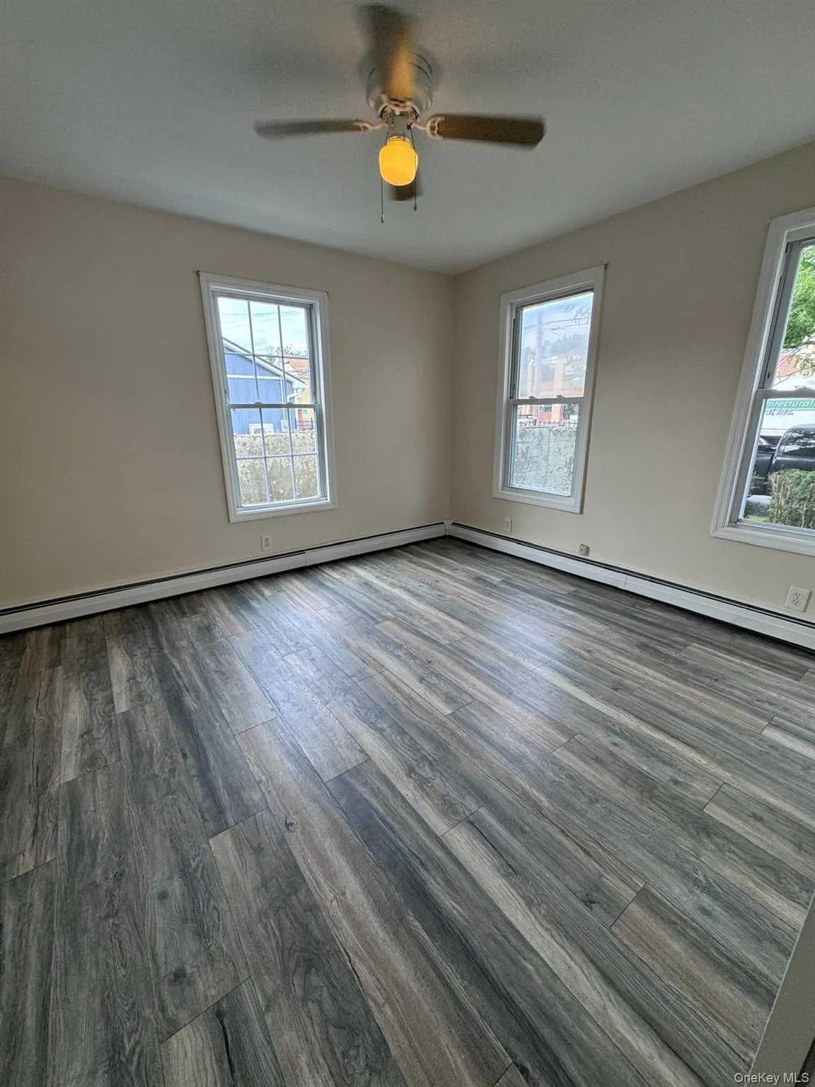 Unfurnished room with wood finished floors, a ceiling fan, and baseboard heating Unfurnished room with wood finished floors, a ceiling fan, and baseboard heating