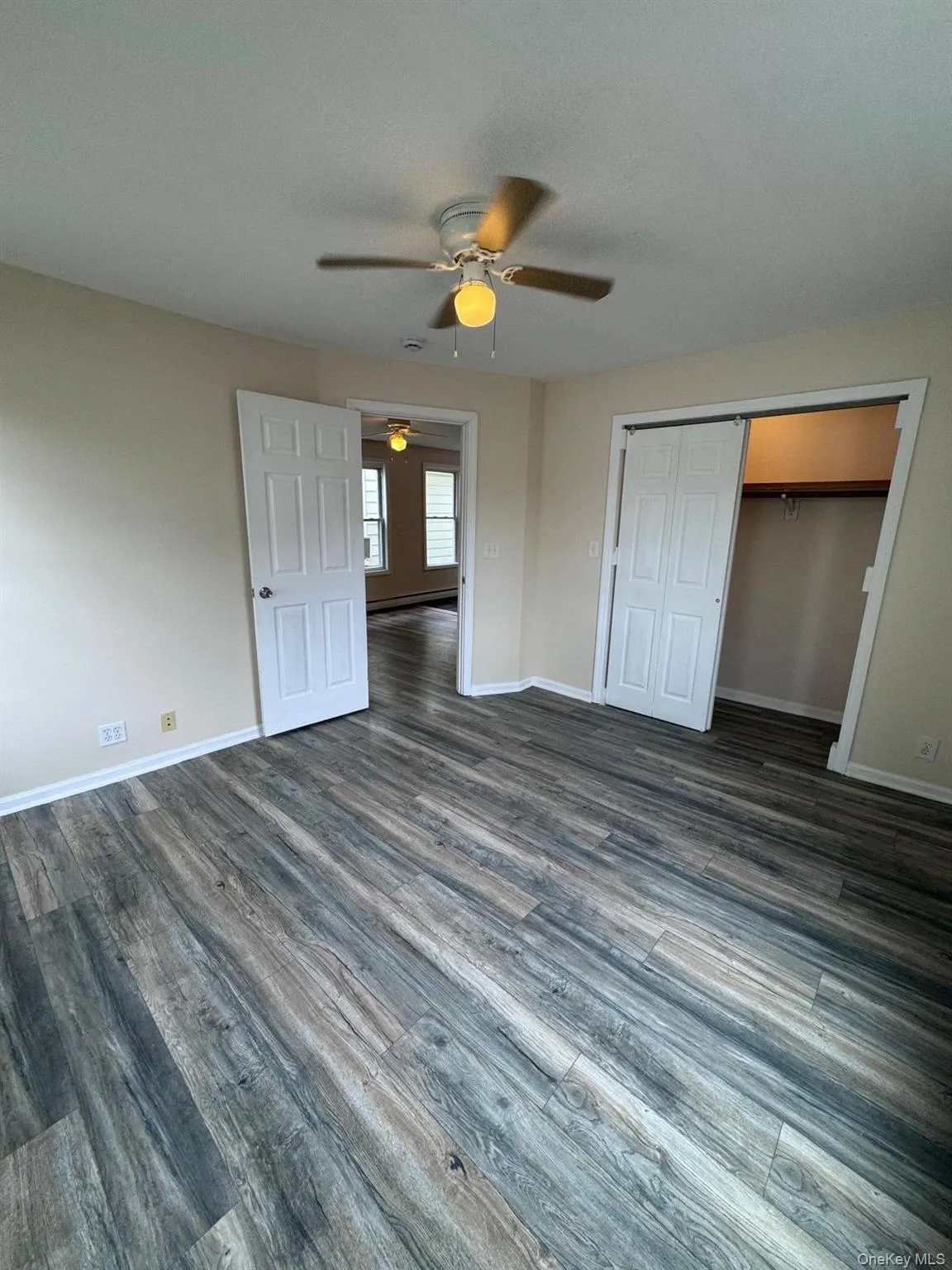 Unfurnished bedroom with dark wood-type flooring, a ceiling fan, a closet, and baseboard heating Unfurnished bedroom with dark wood-type flooring, a ceiling fan, a closet, and baseboard heating