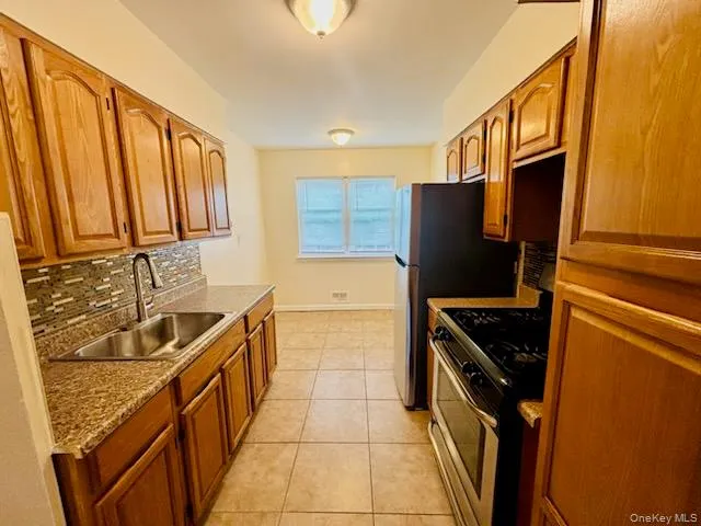 Kitchen with stainless steel appliances, light tile patterned flooring, brown cabinets, and tasteful backsplash Kitchen with stainless steel appliances, light tile patterned flooring, brown cabinets, and tasteful backsplash