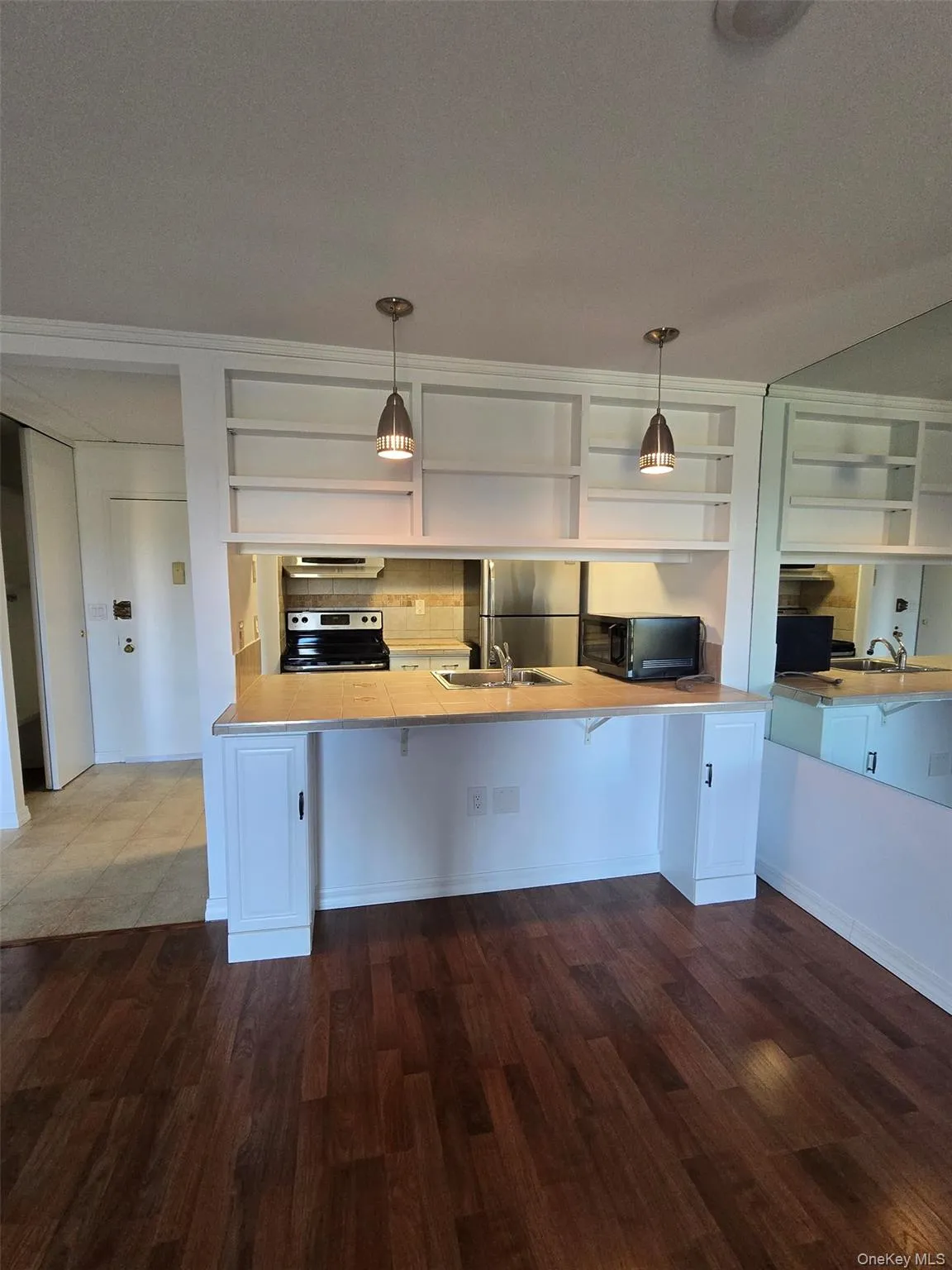 Kitchen with light countertops, open shelves, appliances with stainless steel finishes, decorative light fixtures, and a peninsula Kitchen with light countertops, open shelves, appliances with stainless steel finishes, decorative light fixtures, and a peninsula