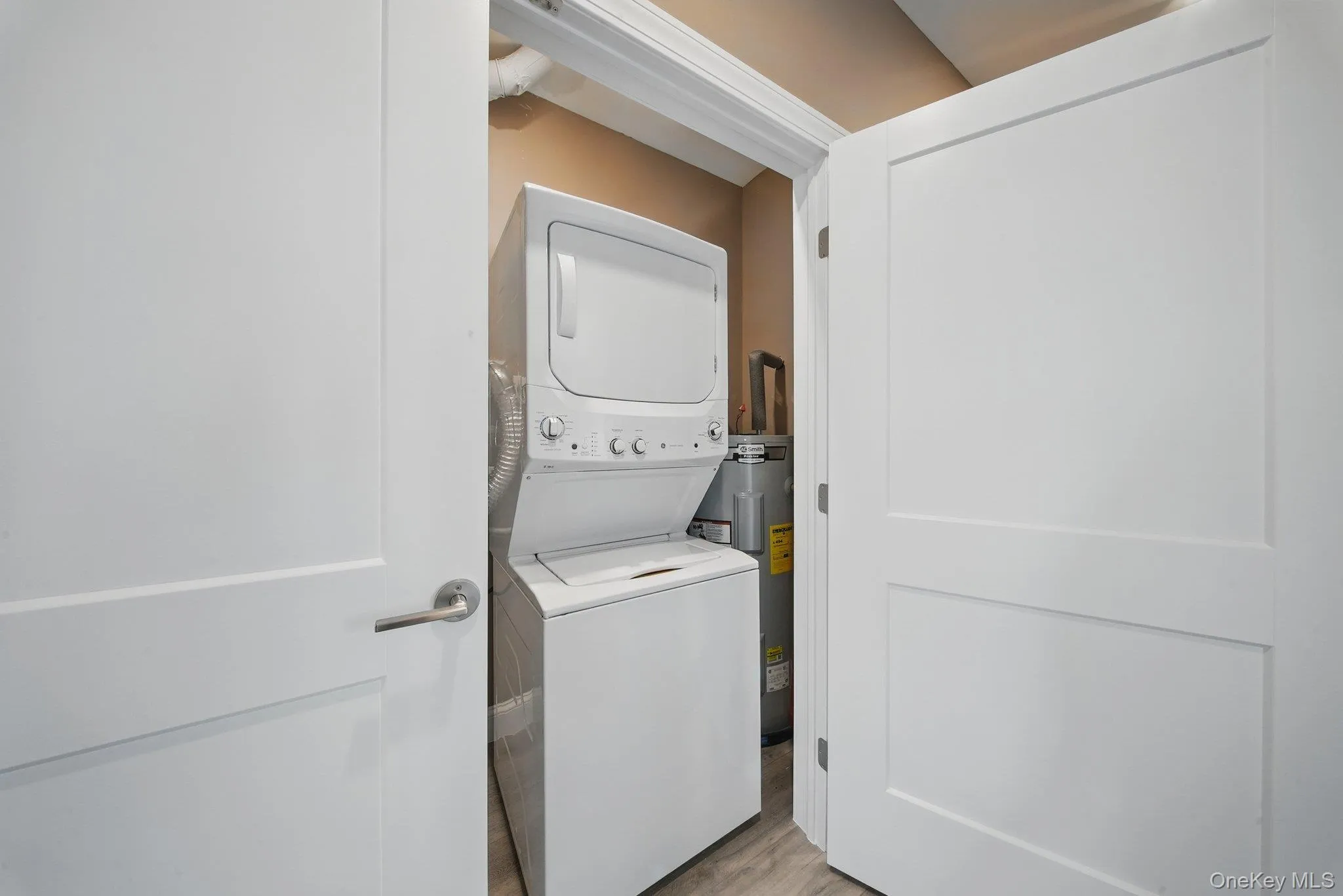 Laundry room with wood finished floors, stacked washing machine and dryer, and water heater Laundry room with wood finished floors, stacked washing machine and dryer, and water heater
