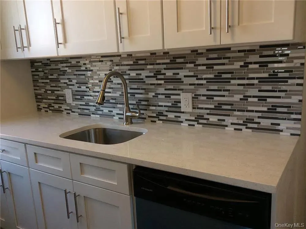 Kitchen with dishwasher, decorative backsplash, light stone countertops, and white cabinets Kitchen with dishwasher, decorative backsplash, light stone countertops, and white cabinets