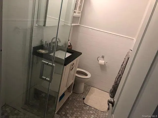 Bathroom featuring tile walls, a stall shower, wainscoting, and vanity Bathroom featuring tile walls, a stall shower, wainscoting, and vanity