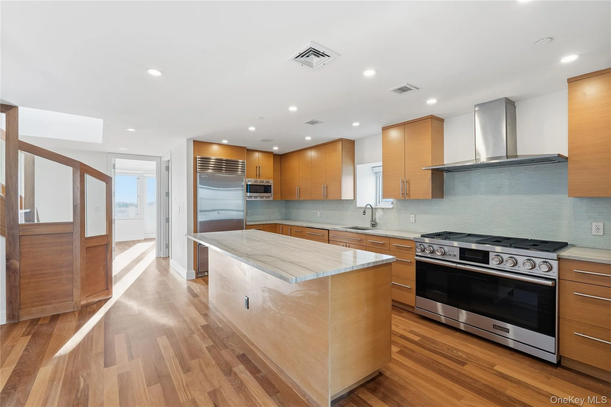 Kitchen featuring built in appliances, wall chimney range hood, tasteful backsplash, modern cabinets, and light stone counters Kitchen featuring built in appliances, wall chimney range hood, tasteful backsplash, modern cabinets, and light stone counters