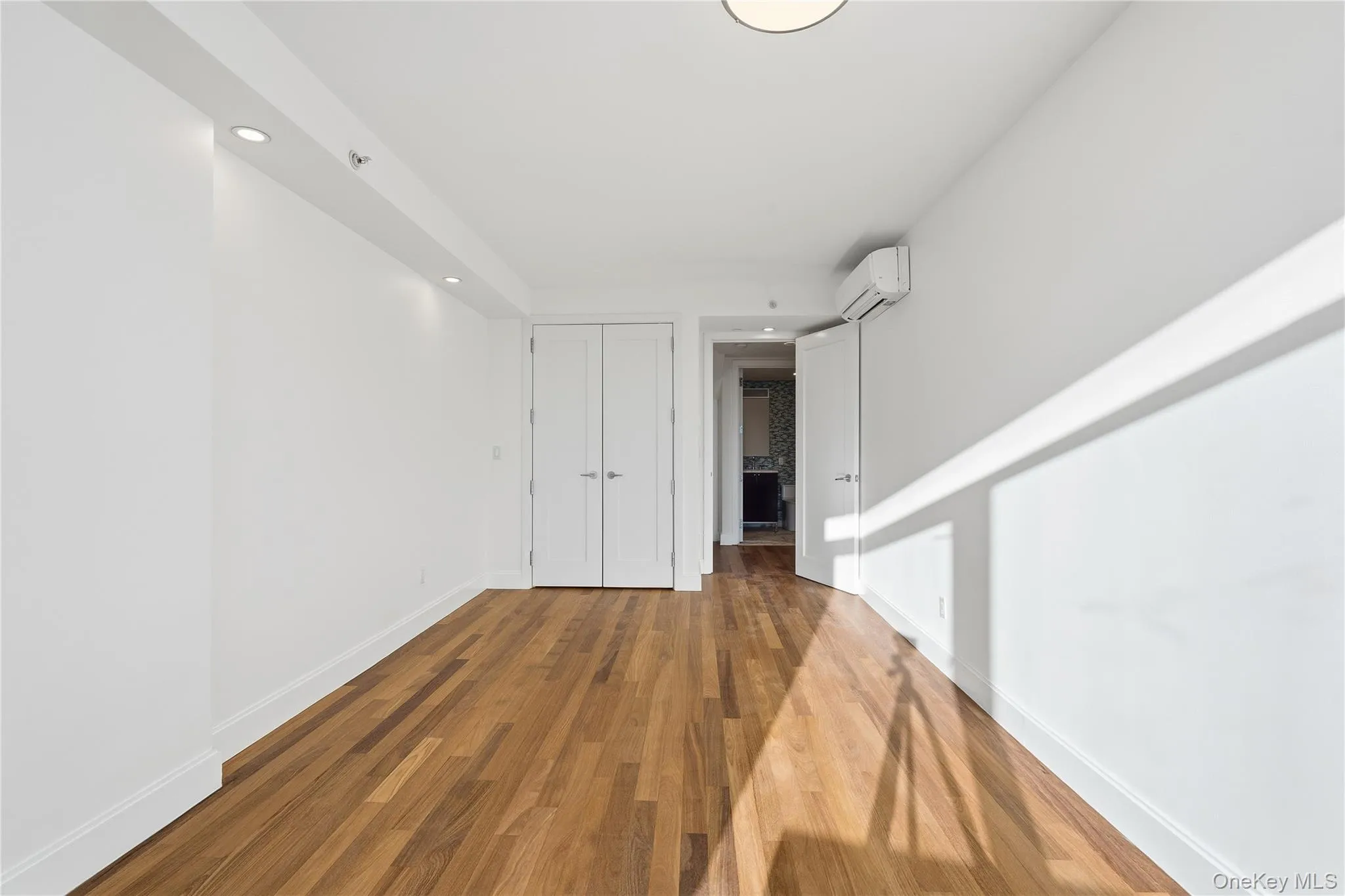 Spare room featuring dark wood-style flooring, recessed lighting, and a wall mounted air conditioner Spare room featuring dark wood-style flooring, recessed lighting, and a wall mounted air conditioner