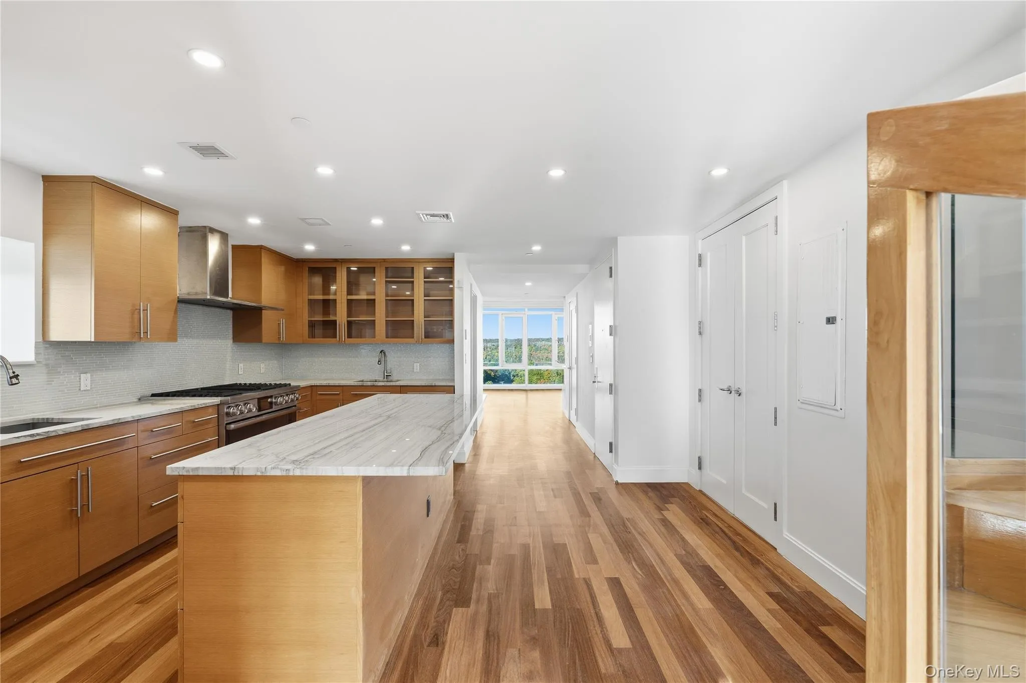 Kitchen with decorative backsplash, glass insert cabinets, light stone counters, a kitchen island, and recessed lighting Kitchen with decorative backsplash, glass insert cabinets, light stone counters, a kitchen island, and recessed lighting