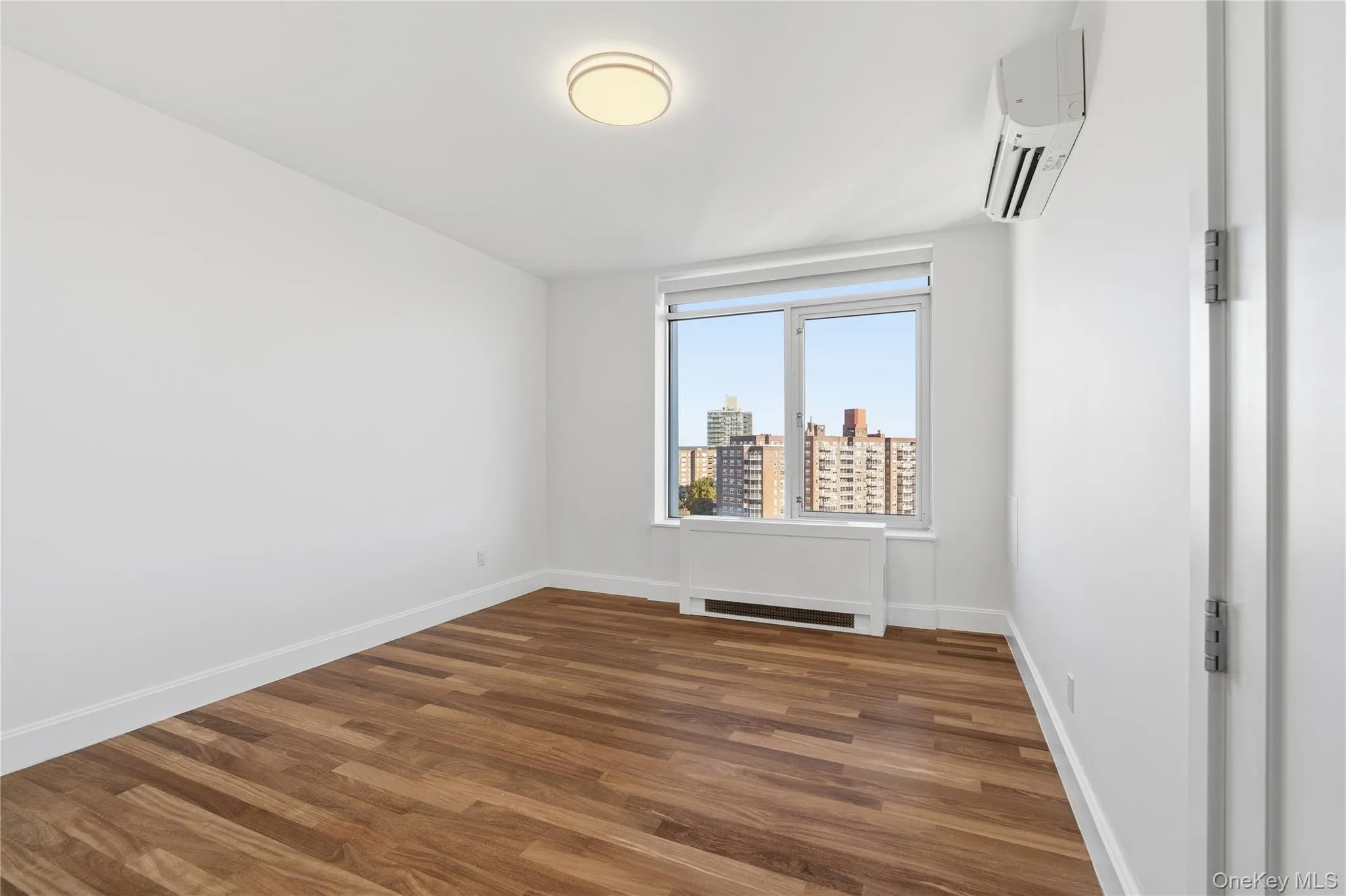 Empty room featuring dark wood finished floors, a view of city, radiator heating unit, and an AC wall unit Empty room featuring dark wood finished floors, a view of city, radiator heating unit, and an AC wall unit