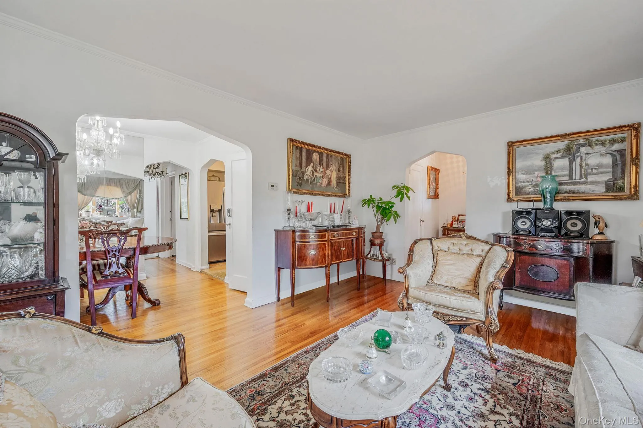 Living area with arched walkways, ornamental molding, wood finished floors, and a chandelier Living area with arched walkways, ornamental molding, wood finished floors, and a chandelier
