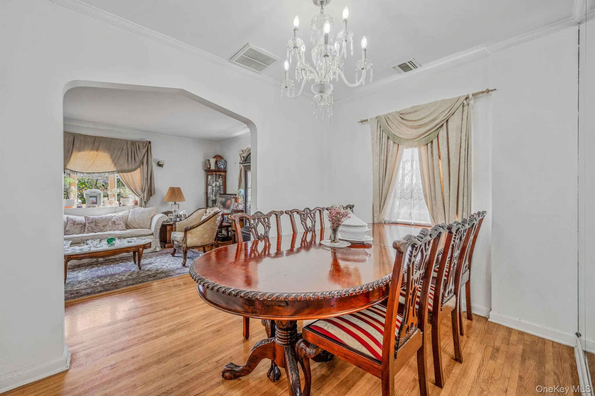 Dining area with arched walkways, light wood-style floors, crown molding, and a chandelier Dining area with arched walkways, light wood-style floors, crown molding, and a chandelier