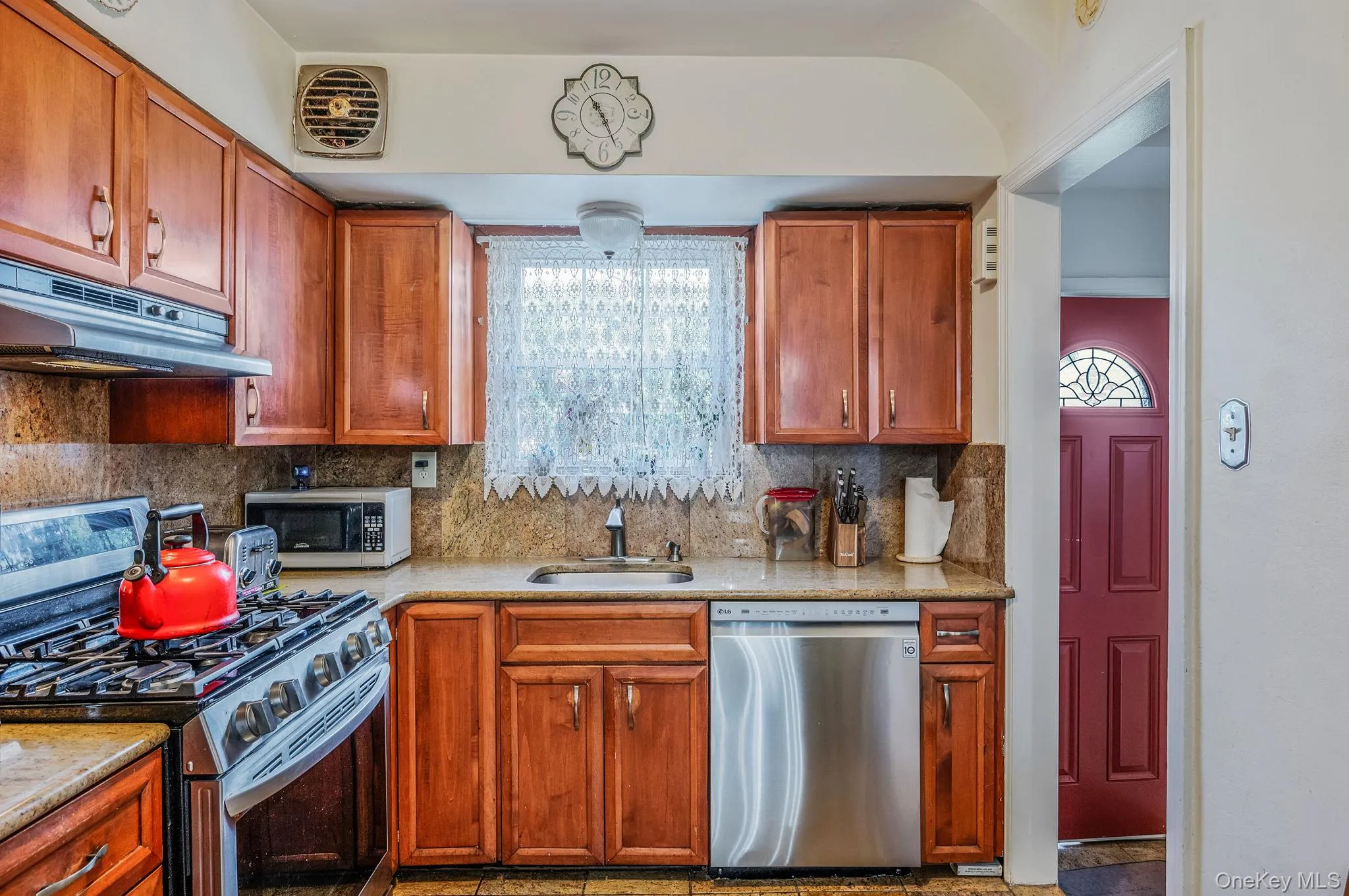 Kitchen with appliances with stainless steel finishes, healthy amount of natural light, decorative backsplash, and light stone countertops Kitchen with appliances with stainless steel finishes, healthy amount of natural light, decorative backsplash, and light stone countertops