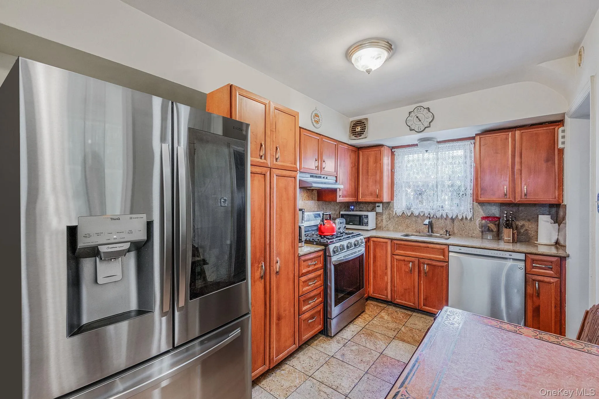 Kitchen with appliances with stainless steel finishes, tasteful backsplash, brown cabinets, under cabinet range hood, and light tile patterned floors Kitchen with appliances with stainless steel finishes, tasteful backsplash, brown cabinets, under cabinet range hood, and light tile patterned floors