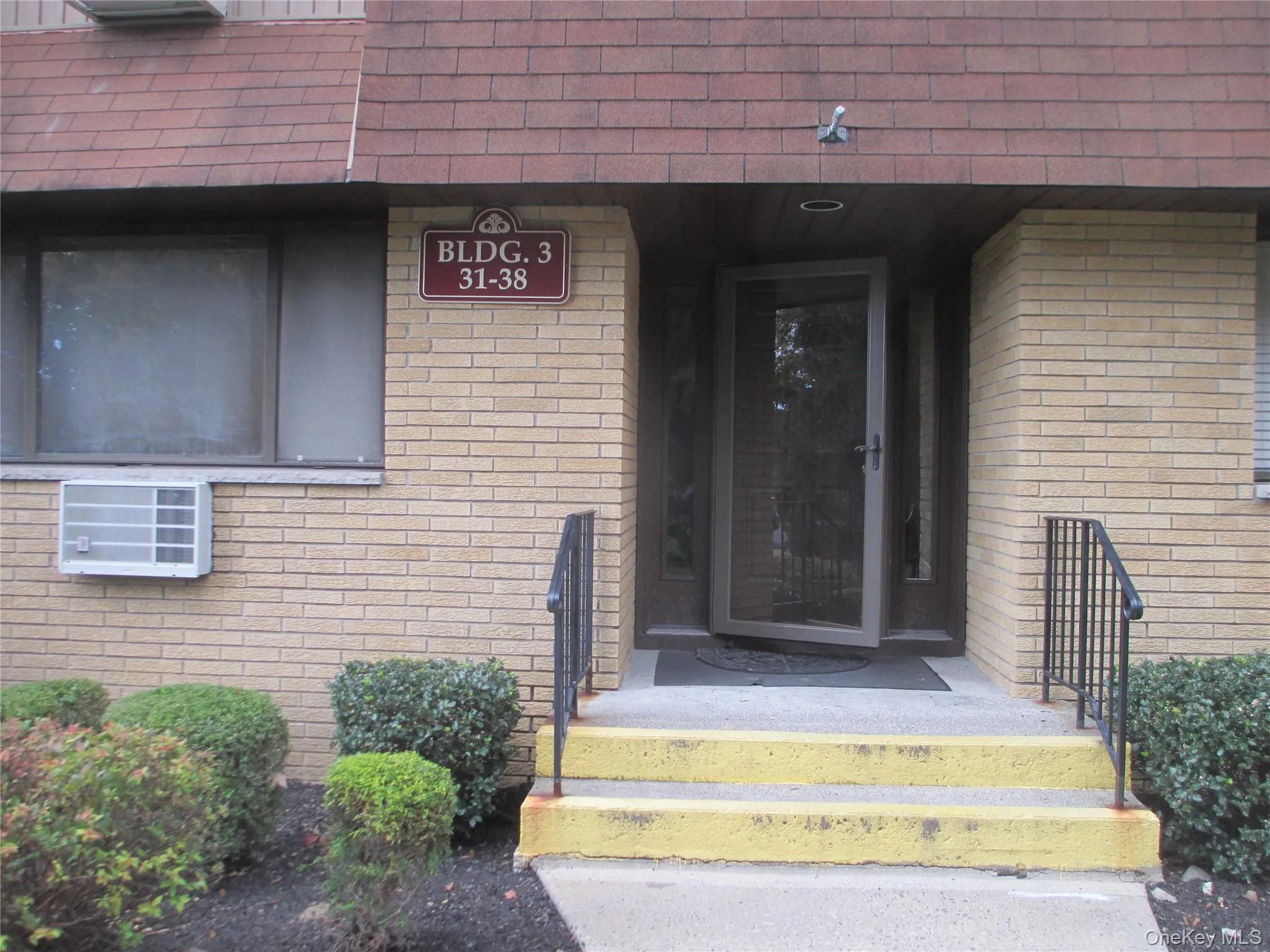Doorway to property with brick siding, mansard roof, and roof with shingles Doorway to property with brick siding, mansard roof, and roof with shingles