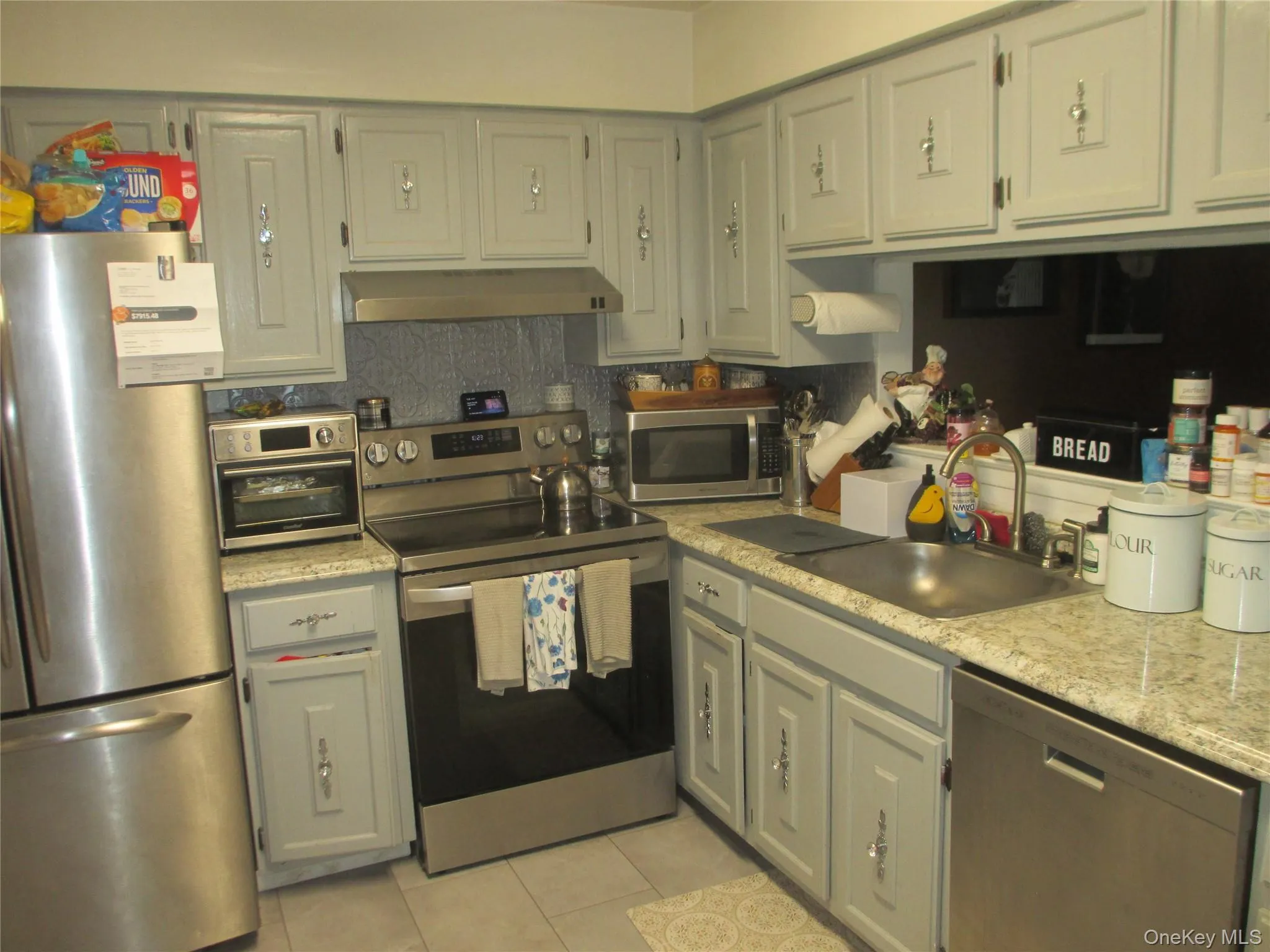 Kitchen featuring stainless steel appliances, light countertops, light tile patterned floors, decorative backsplash, and under cabinet range hood Kitchen featuring stainless steel appliances, light countertops, light tile patterned floors, decorative backsplash, and under cabinet range hood