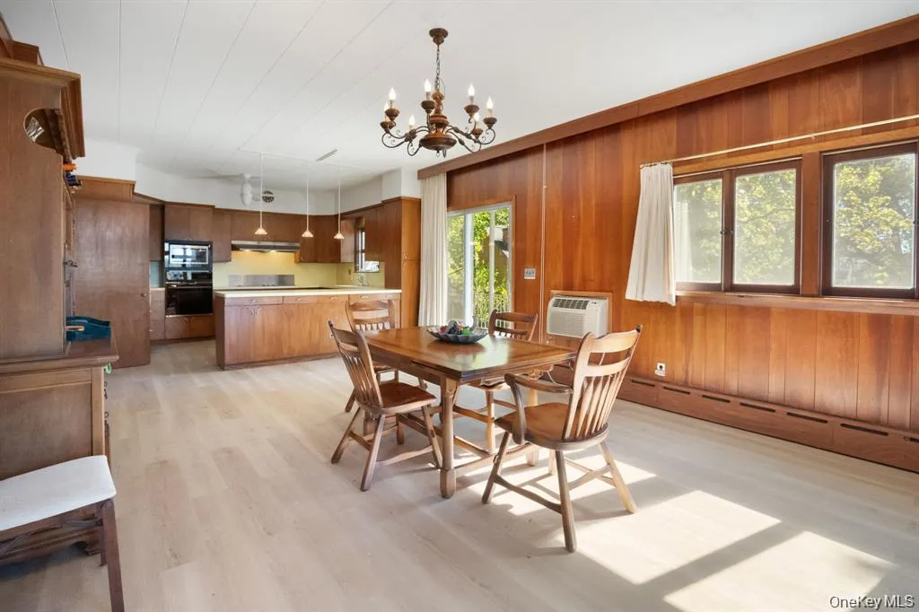 Dining space featuring a chandelier, light wood-style flooring, baseboard heating, wood walls, and a wall mounted air conditioner Dining space featuring a chandelier, light wood-style flooring, baseboard heating, wood walls, and a wall mounted air conditioner