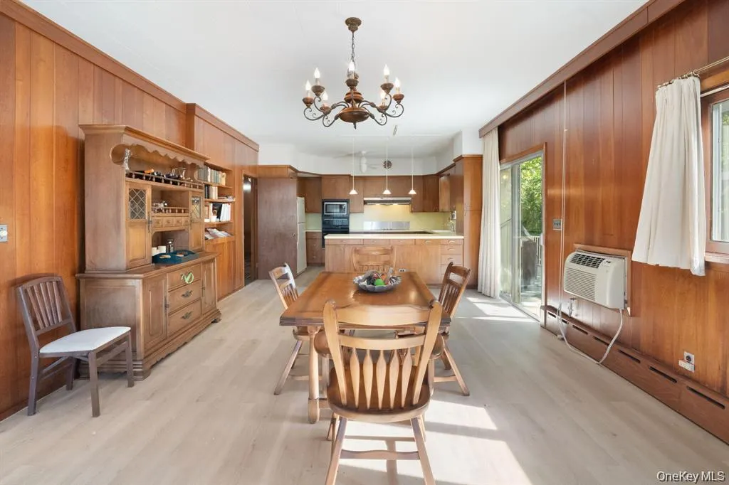 Dining area with wood walls, a chandelier, baseboard heating, light wood-style flooring, and a wall unit AC Dining area with wood walls, a chandelier, baseboard heating, light wood-style flooring, and a wall unit AC