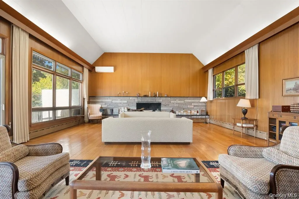 Living area featuring wooden walls, light wood-style floors, vaulted ceiling, a baseboard heating unit, and a wall unit AC Living area featuring wooden walls, light wood-style floors, vaulted ceiling, a baseboard heating unit, and a wall unit AC
