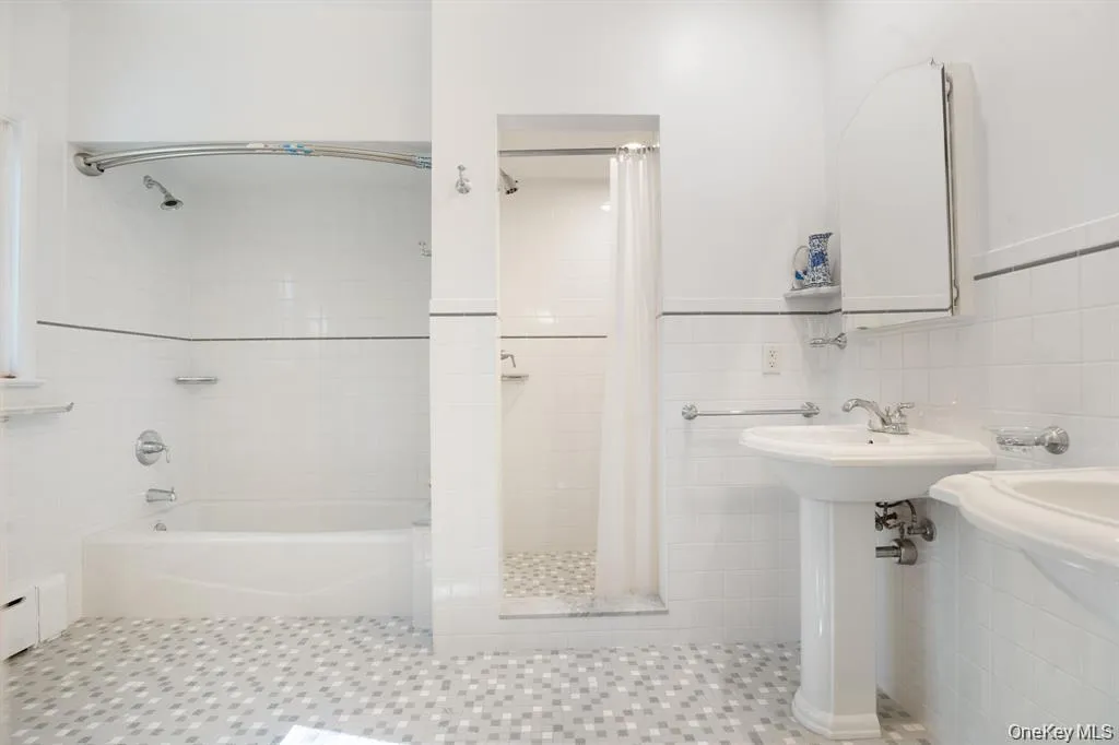 Bathroom featuring tile walls, baseboard heating, shower / bath combo with shower curtain, and tile patterned floors Bathroom featuring tile walls, baseboard heating, shower / bath combo with shower curtain, and tile patterned floors