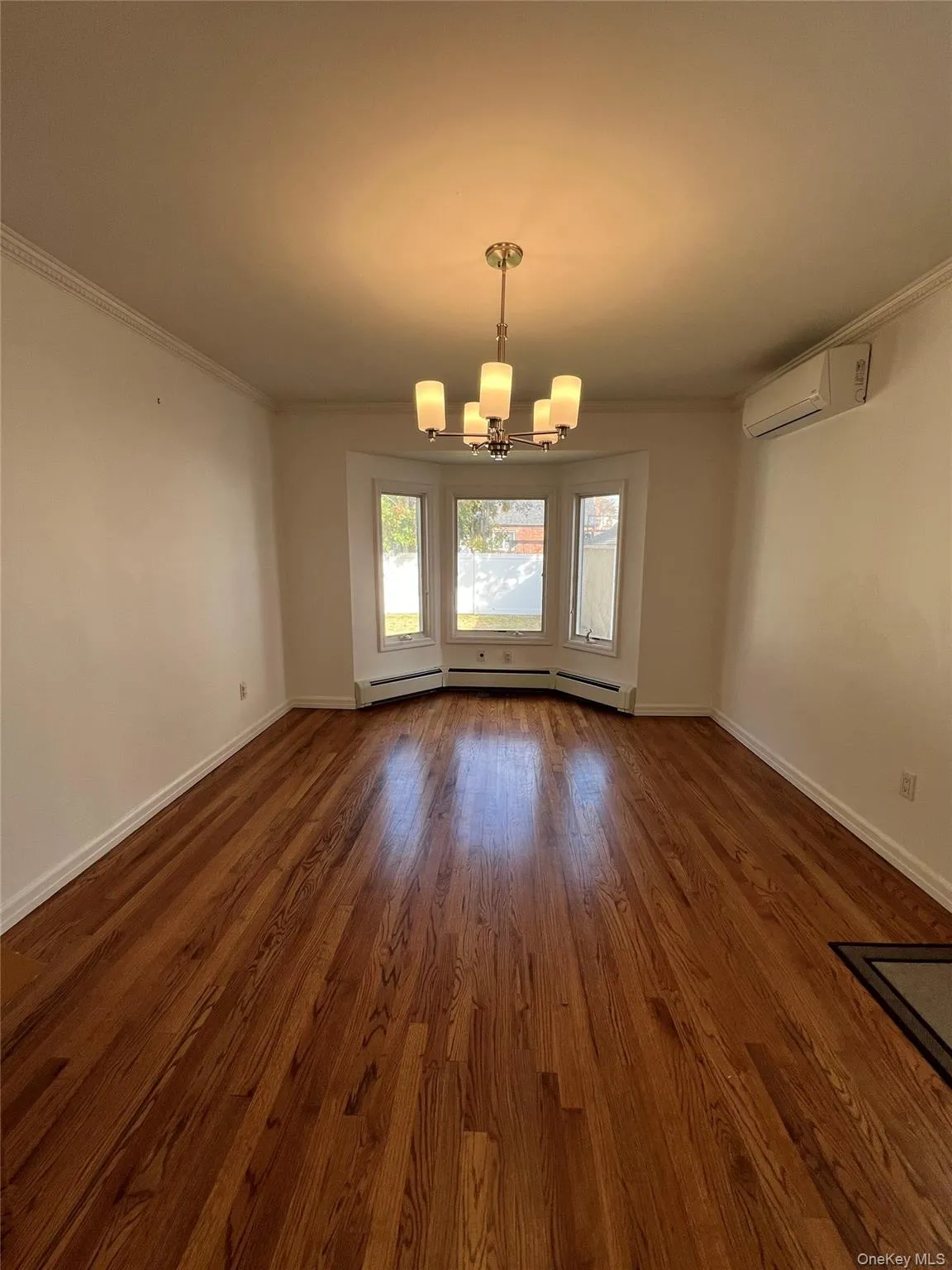 Unfurnished dining area featuring crown molding, a chandelier, dark wood finished floors, baseboard heating, and an AC wall unit Unfurnished dining area featuring crown molding, a chandelier, dark wood finished floors, baseboard heating, and an AC wall unit