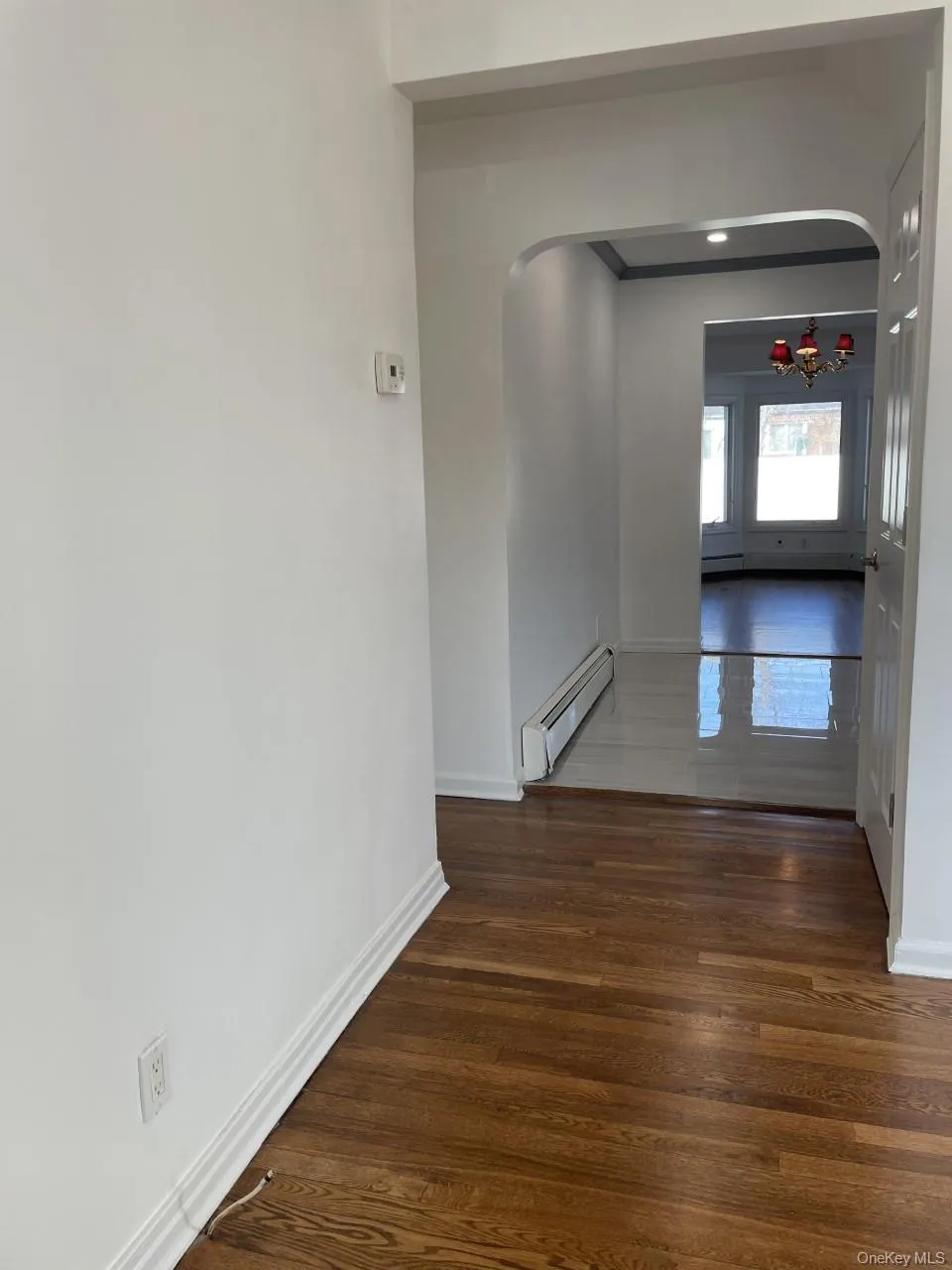 Corridor featuring arched walkways, dark wood-type flooring, and baseboard heating Corridor featuring arched walkways, dark wood-type flooring, and baseboard heating