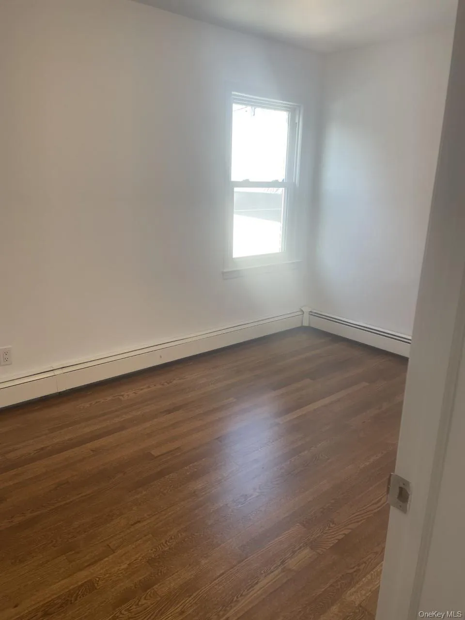 Empty room featuring dark wood-style floors and a baseboard radiator Empty room featuring dark wood-style floors and a baseboard radiator