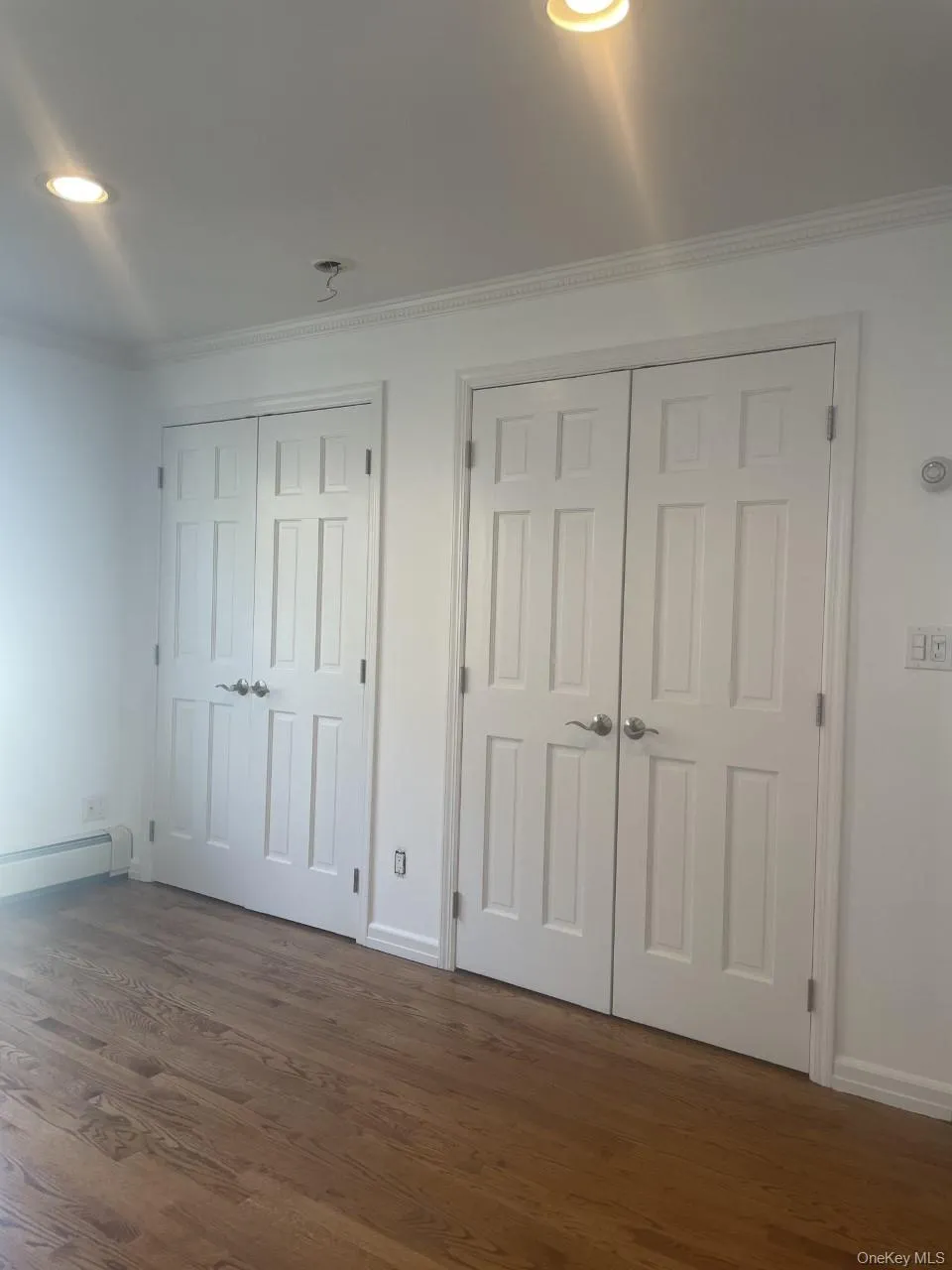 Unfurnished bedroom with multiple closets, crown molding, baseboard heating, dark wood finished floors, and recessed lighting Unfurnished bedroom with multiple closets, crown molding, baseboard heating, dark wood finished floors, and recessed lighting