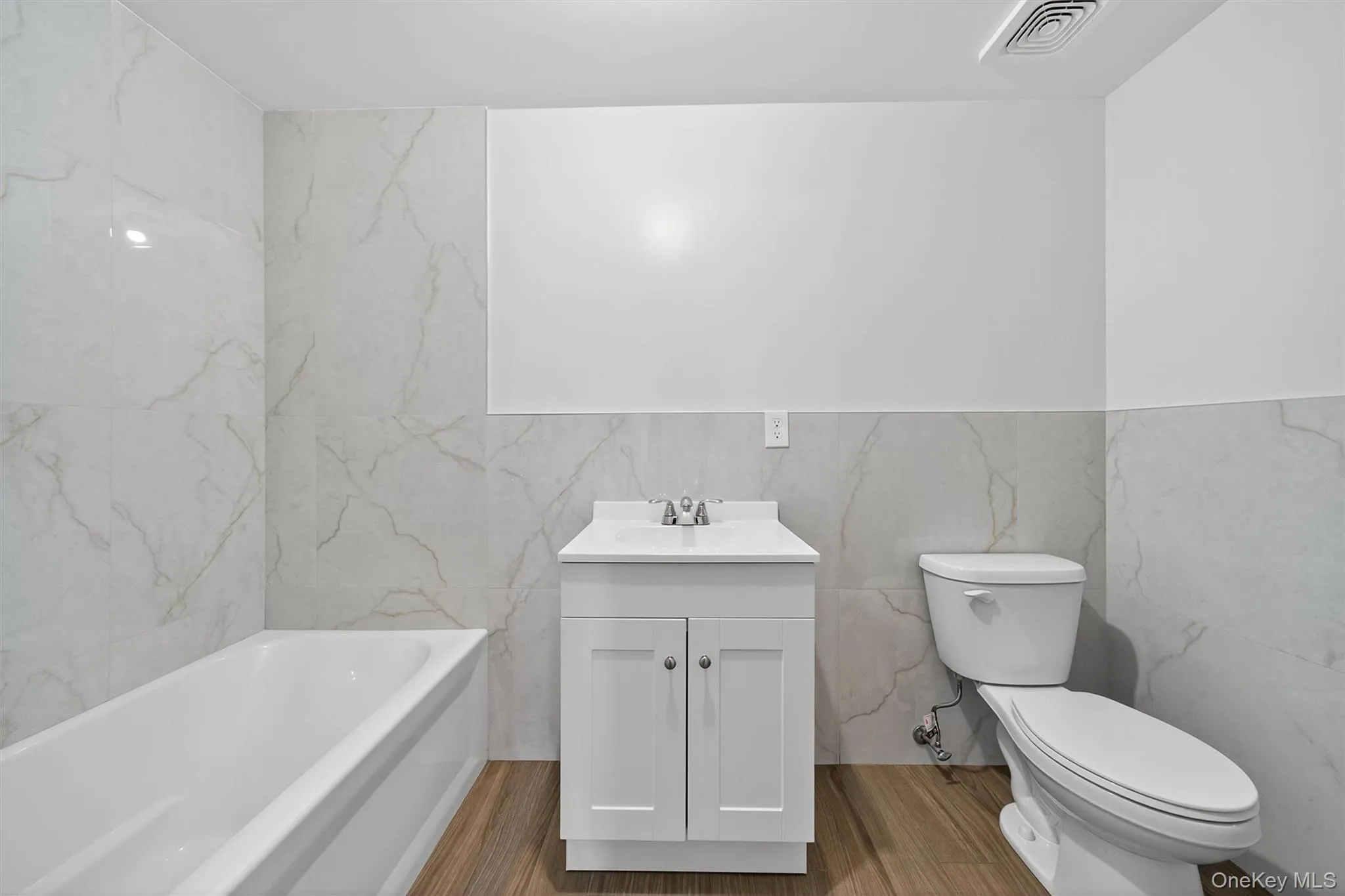 Full bathroom with vanity, light wood finished floors, tile walls, and a bath Full bathroom with vanity, light wood finished floors, tile walls, and a bath