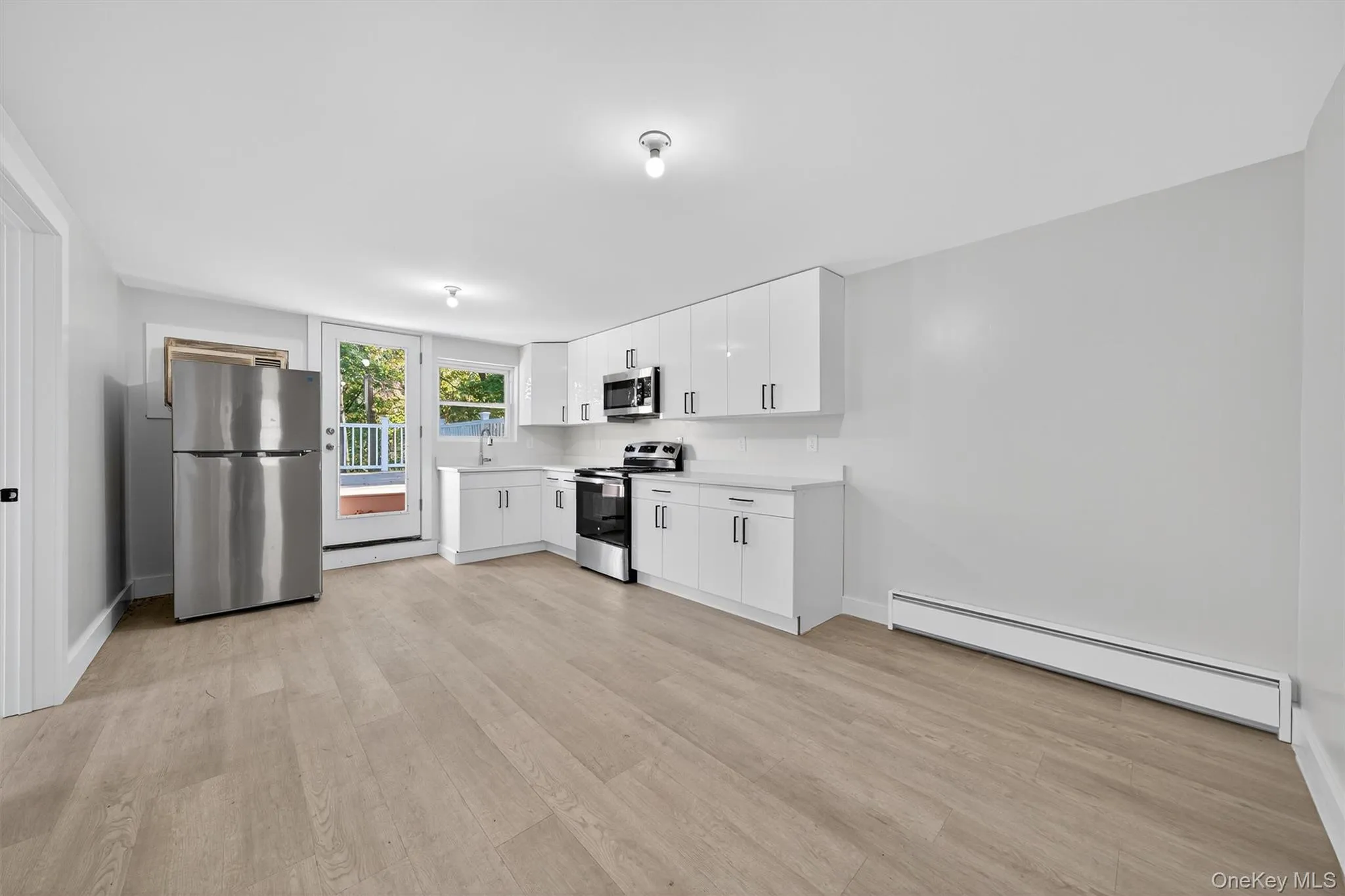 Kitchen with a baseboard radiator, appliances with stainless steel finishes, white cabinetry, light countertops, and light wood-style floors Kitchen with a baseboard radiator, appliances with stainless steel finishes, white cabinetry, light countertops, and light wood-style floors
