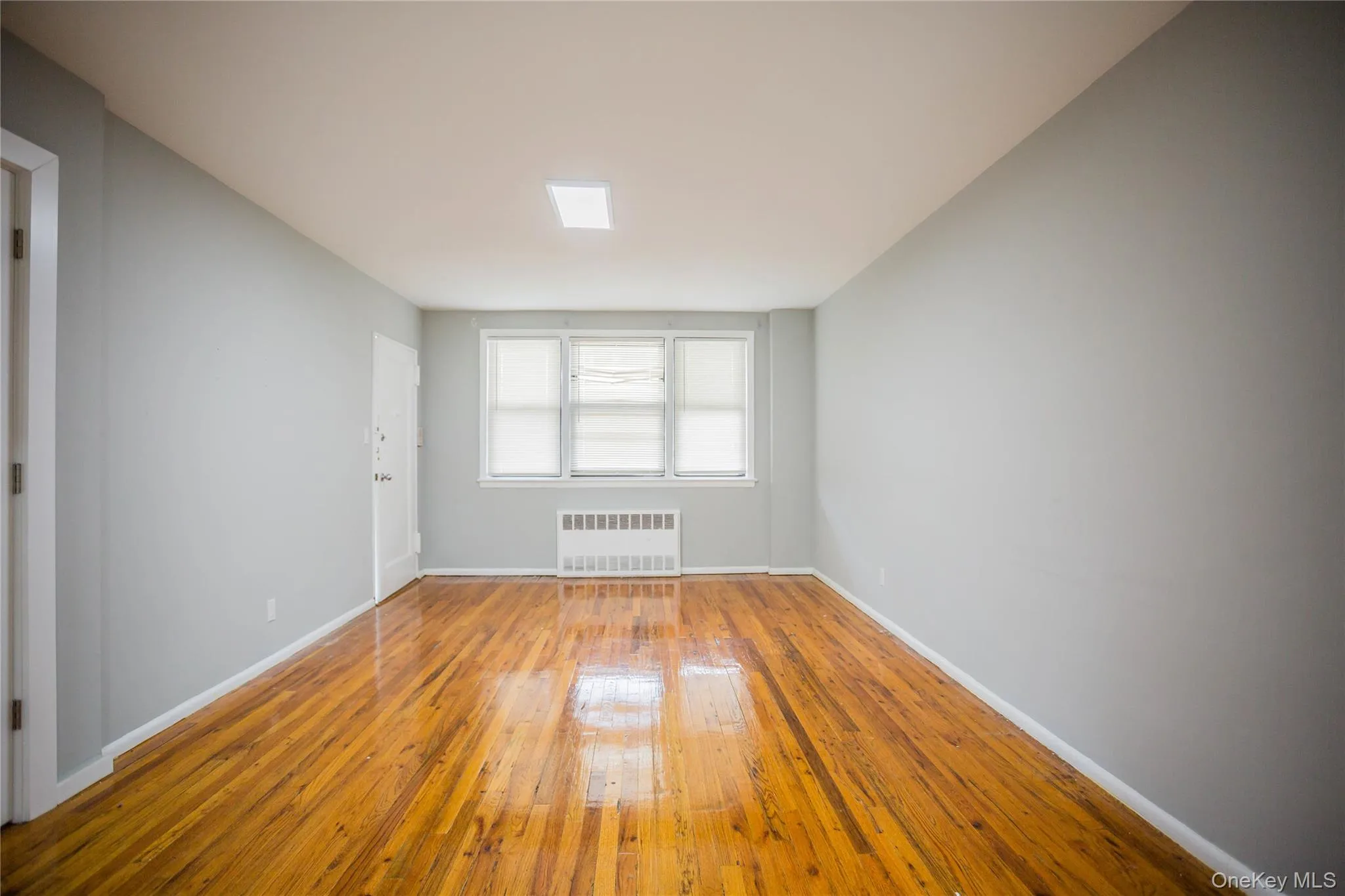 Empty room featuring hardwood / wood-style flooring and radiator heating unit Empty room featuring hardwood / wood-style flooring and radiator heating unit