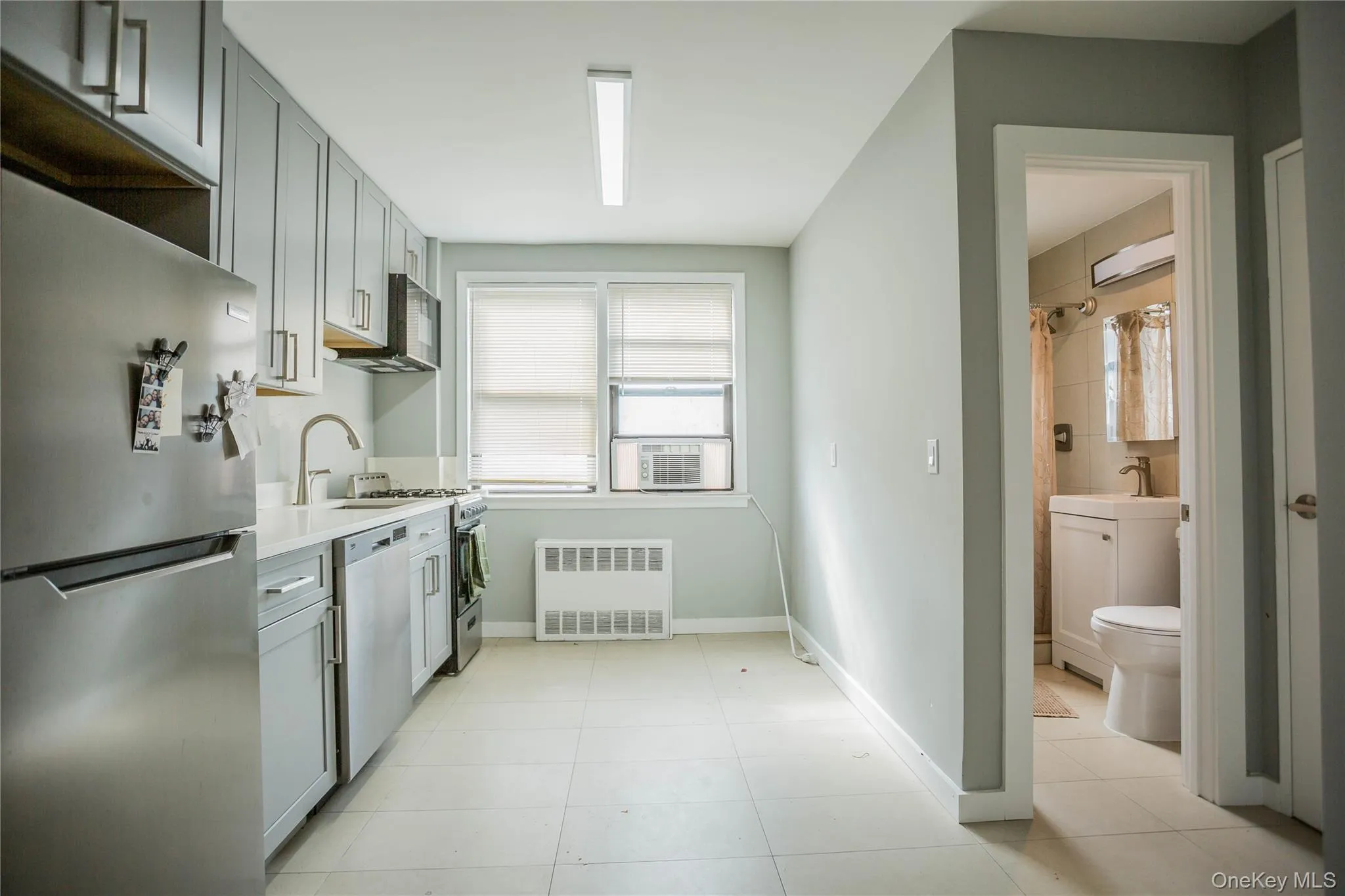 Kitchen with appliances with stainless steel finishes, gray cabinetry, radiator heating unit, and light tile patterned flooring Kitchen with appliances with stainless steel finishes, gray cabinetry, radiator heating unit, and light tile patterned flooring